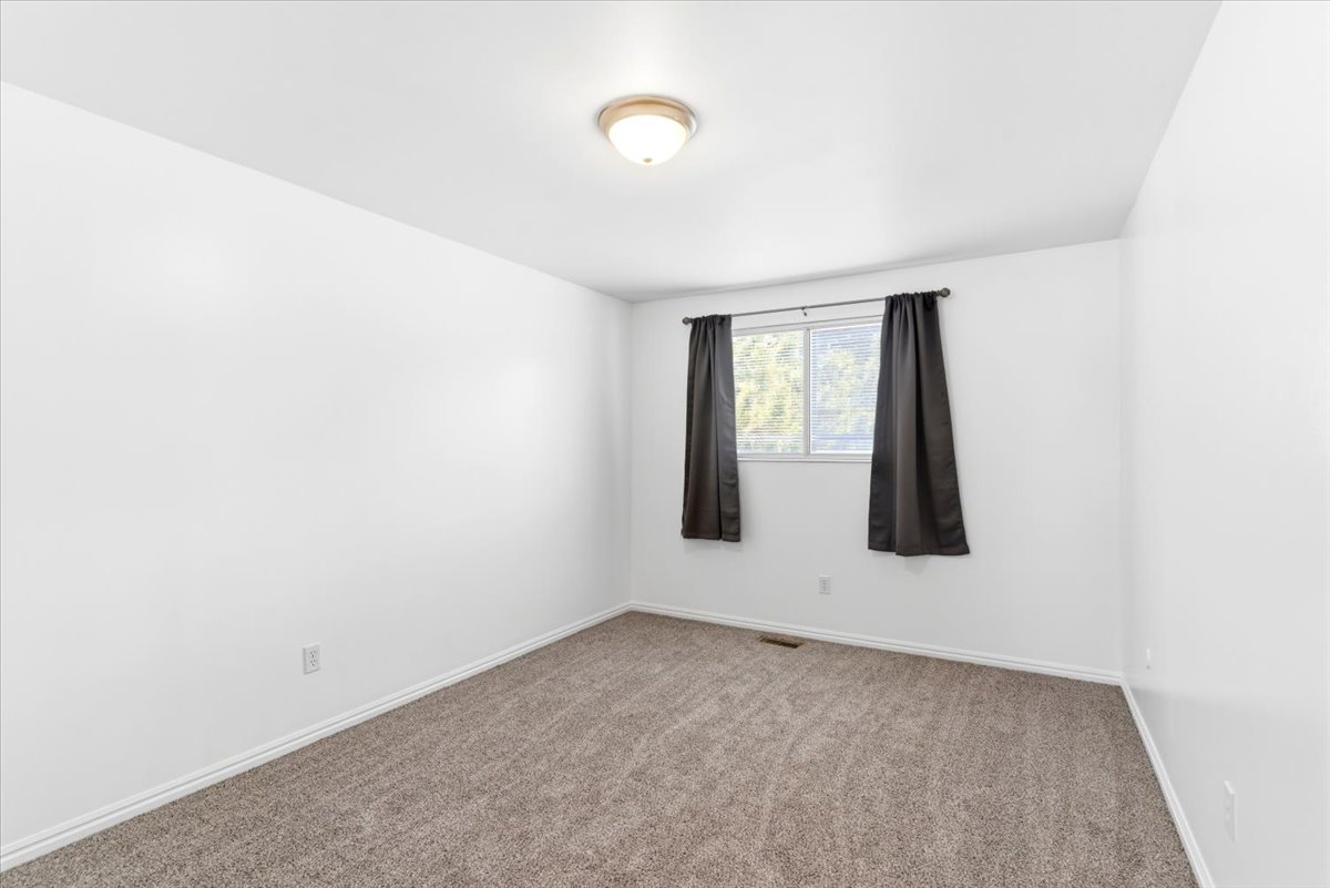 Room featuring neutral-toned carpet, white walls, and a single window with dark drapery