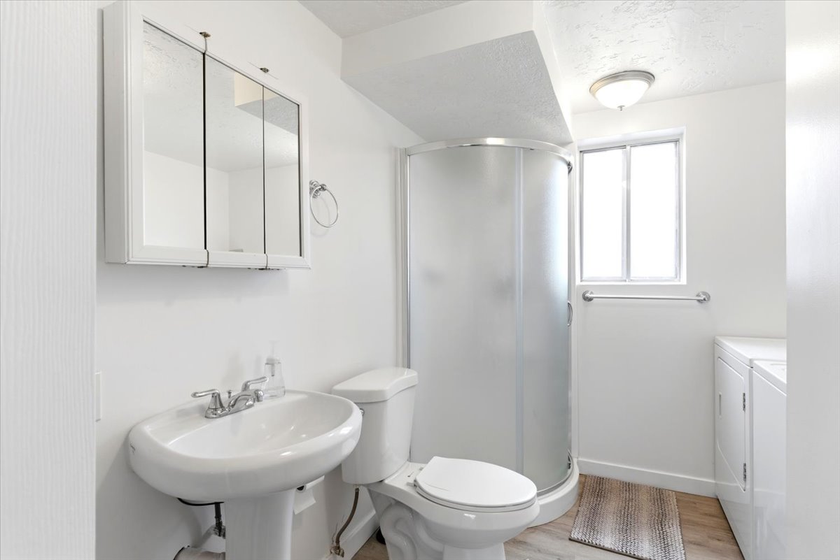 Compact bathroom featuring a pedestal sink, three-door mirrored medicine cabinet, and a rounded shower enclosure