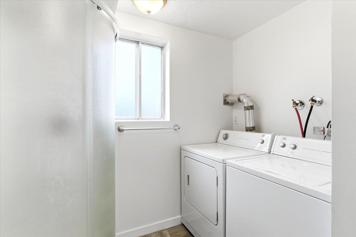 Dedicated laundry area featuring a side-by-side washer and dryer, frosted window, overhead lighting, and wood-finish flooring