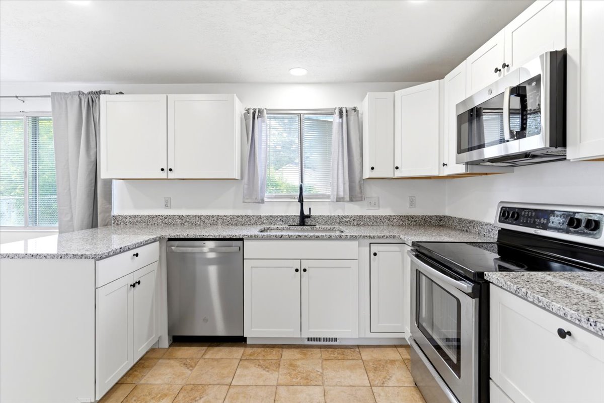 Kitchen featuring white shaker-style cabinetry, speckled countertops, stainless steel appliances, and tiled flooring