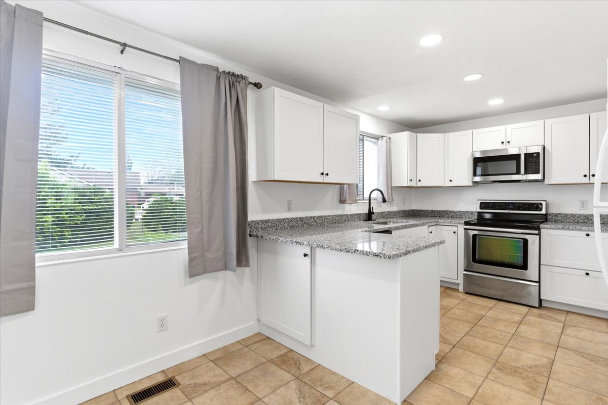 Kitchen featuring white cabinetry, stainless steel appliances, granite-style countertops, and tile flooring