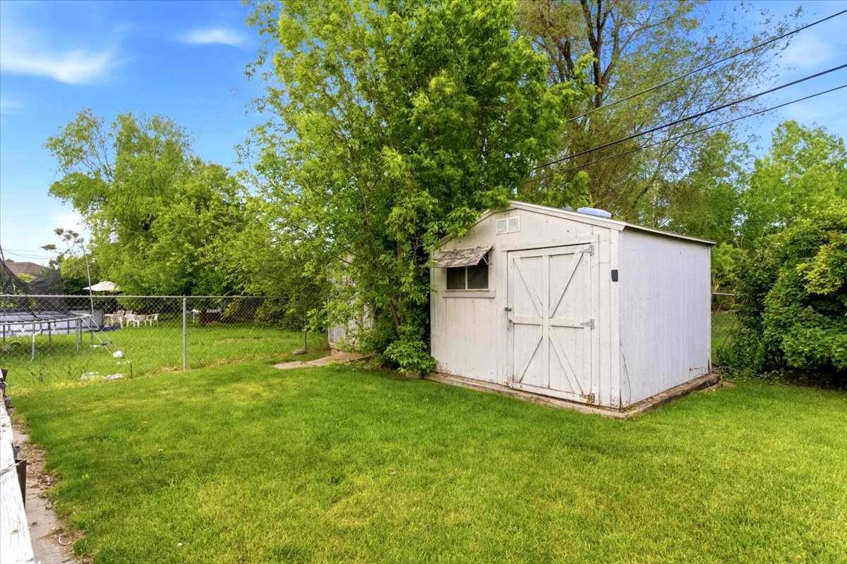 Expansive lawn featuring mature trees and a detached shed with a window and double doors