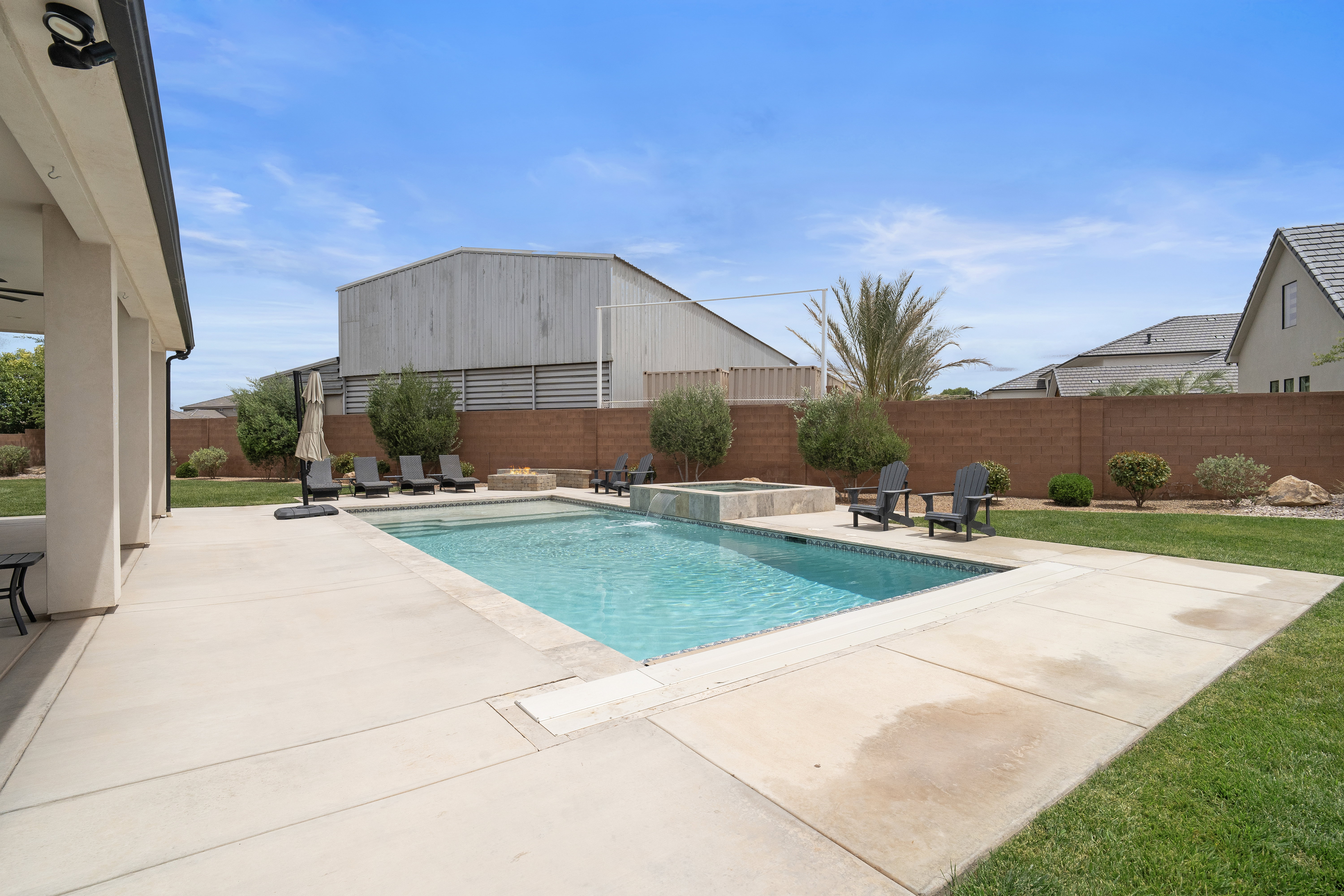 Expansive backyard featuring a rectangular swimming pool, integrated spa, fire pit, and mature perimeter landscaping.