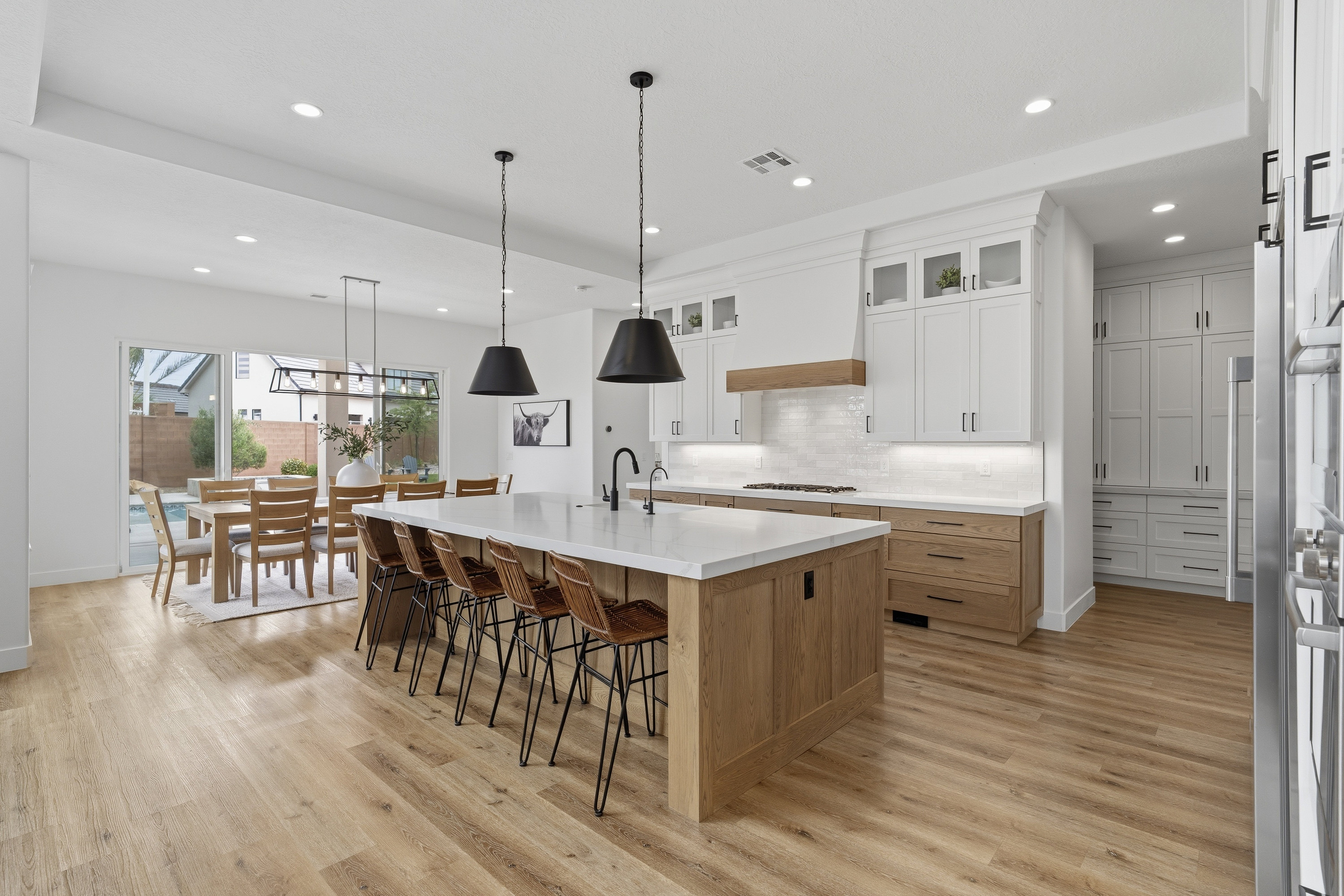 Open-concept kitchen featuring a large central island with seating, stone countertops, wood-finish flooring, white upper cabinetry, and wood-finish lower cabinetry.