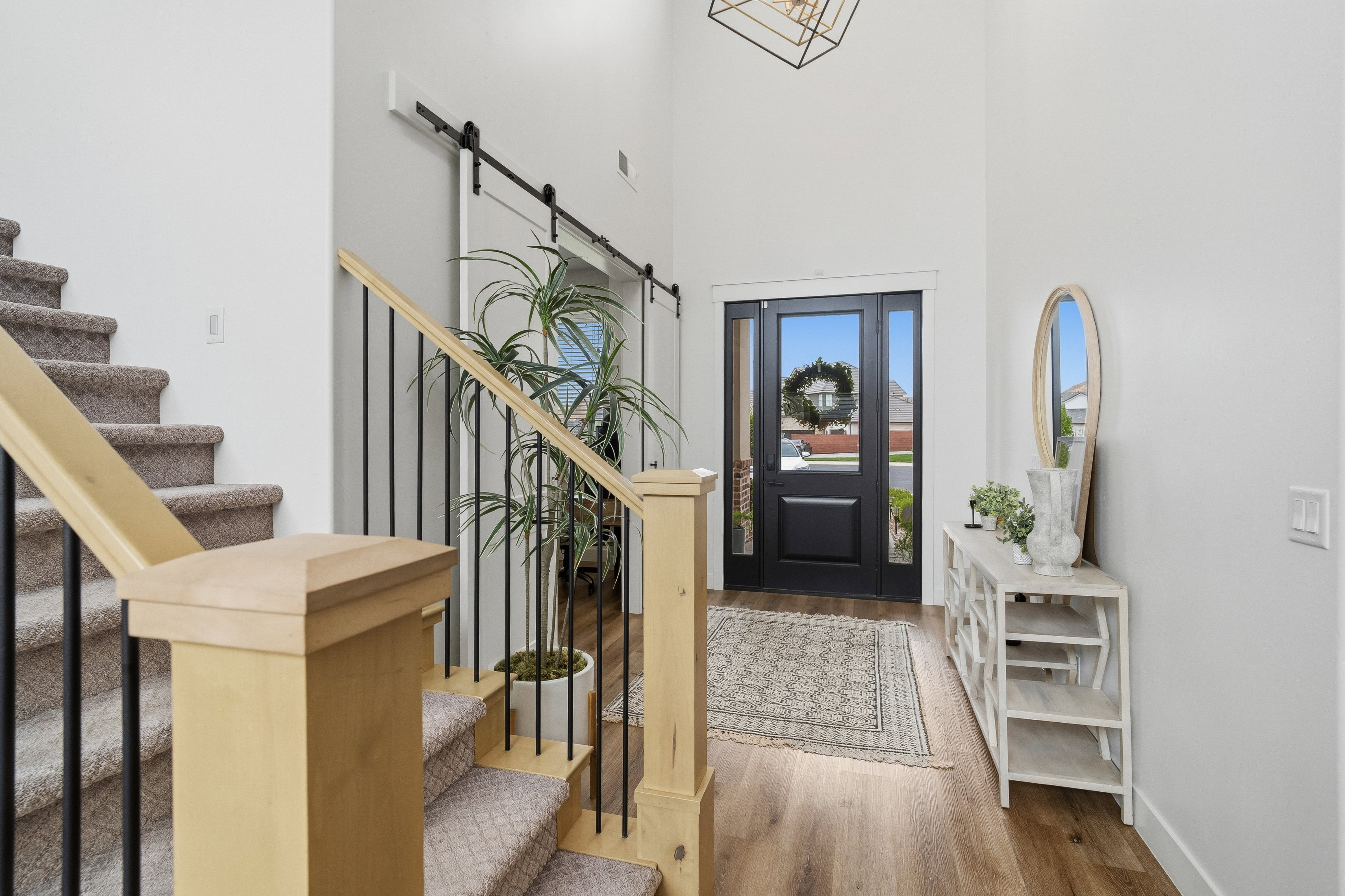 Foyer featuring a tall ceiling, wood-finish flooring, a dark entry door with glass panels, and a contrasting light wood staircase with black metal balusters.