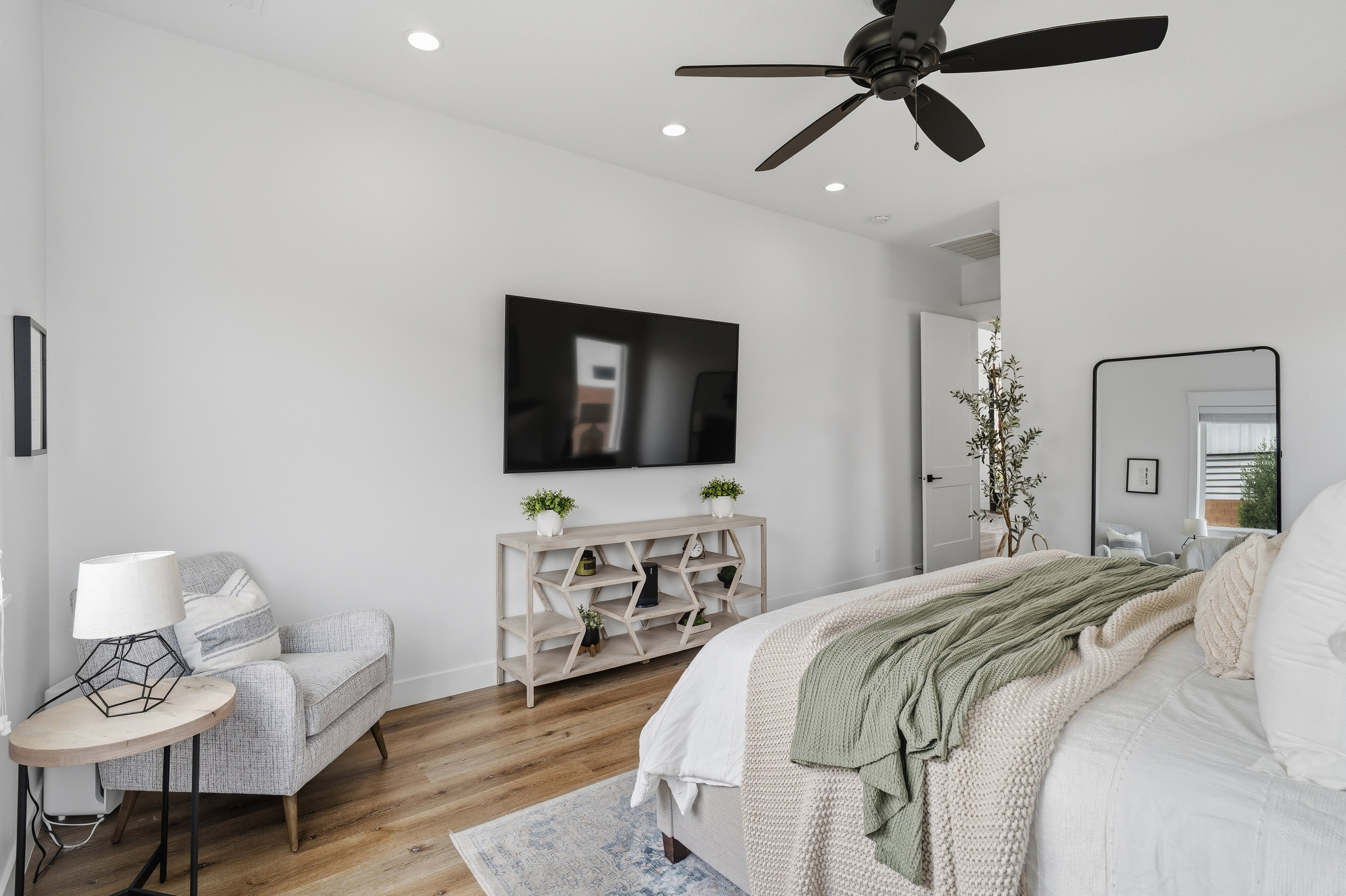 Spacious bedroom featuring light wood-finish flooring, recessed lighting, and a modern ceiling fan.