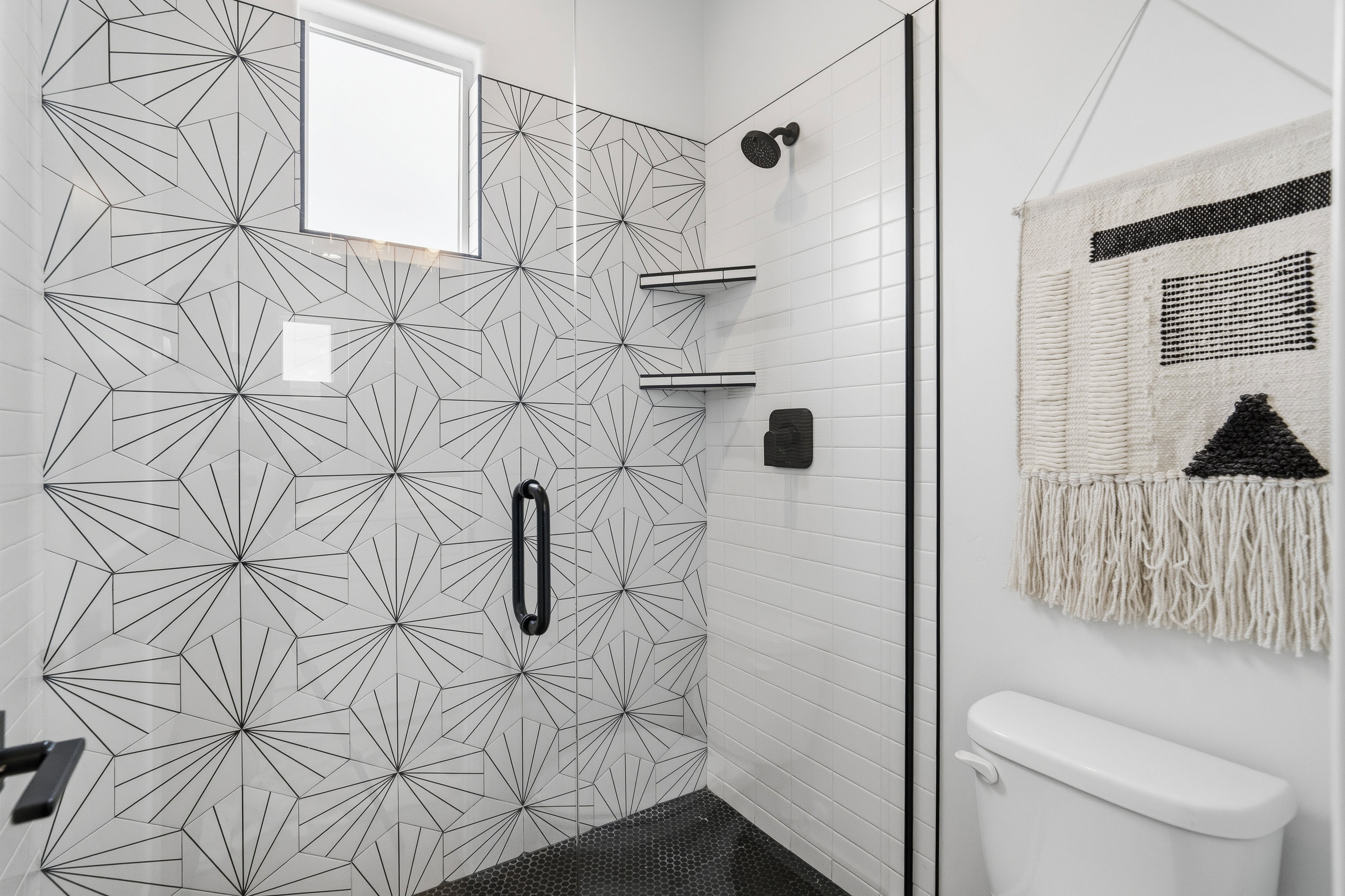 Walk-in shower with geometric patterned tile accent wall, black hexagonal floor tile, and matte black fixtures.