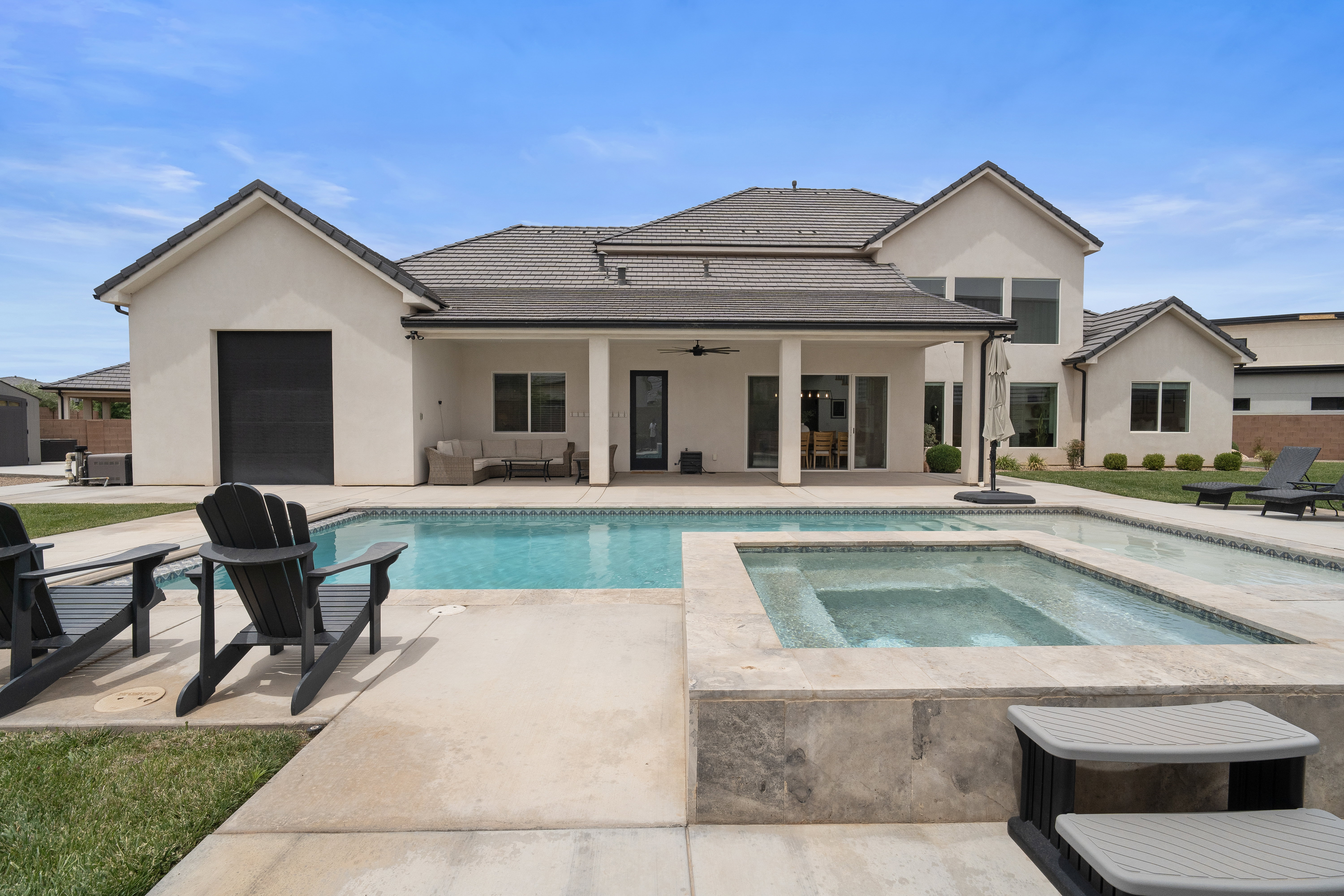 Expansive backyard featuring a rectangular swimming pool, an integrated spa with stone surround, a covered patio with recessed lighting, and a stucco exterior.