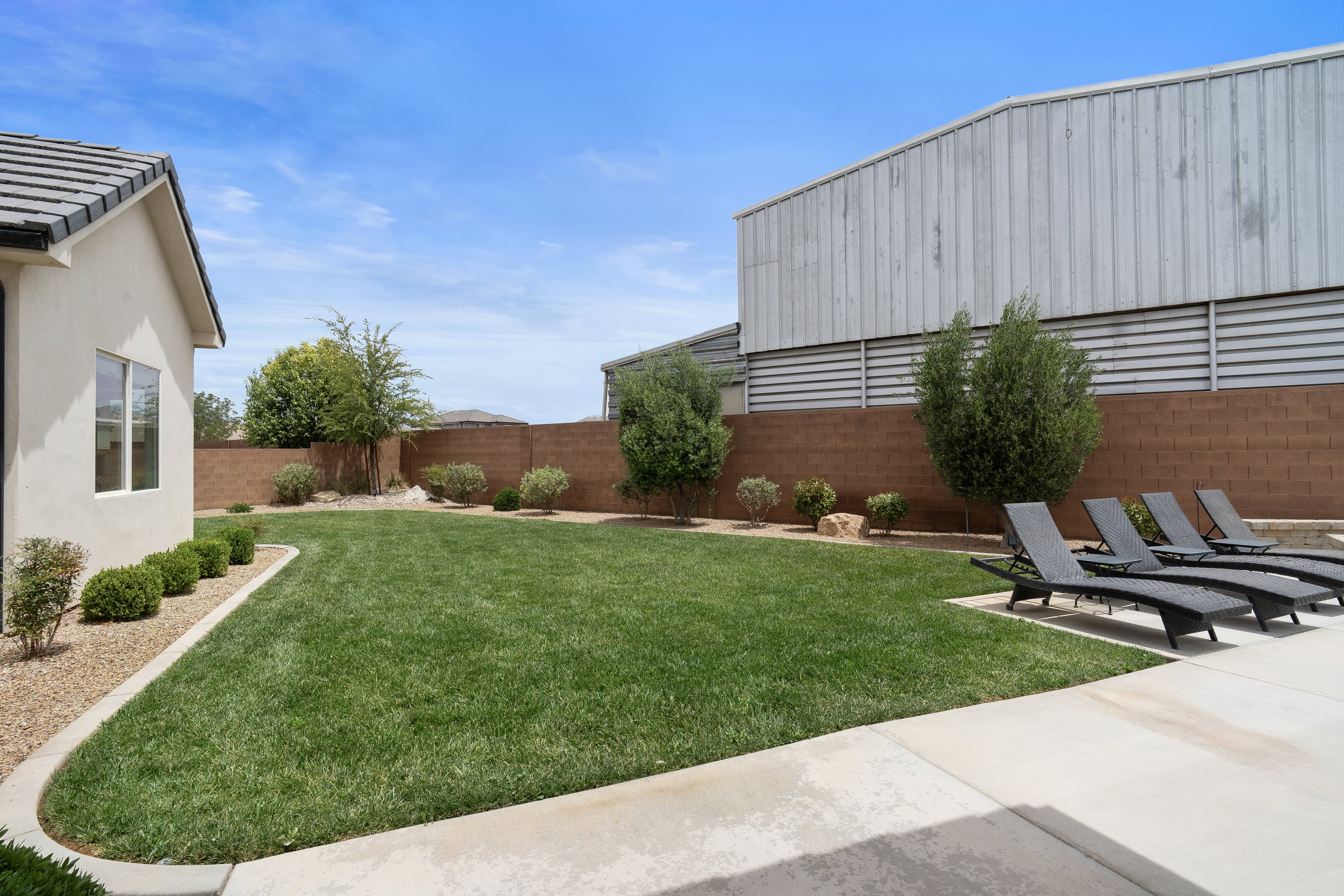 Expansive green lawn with mature landscaping, a concrete patio, and a block wall perimeter.