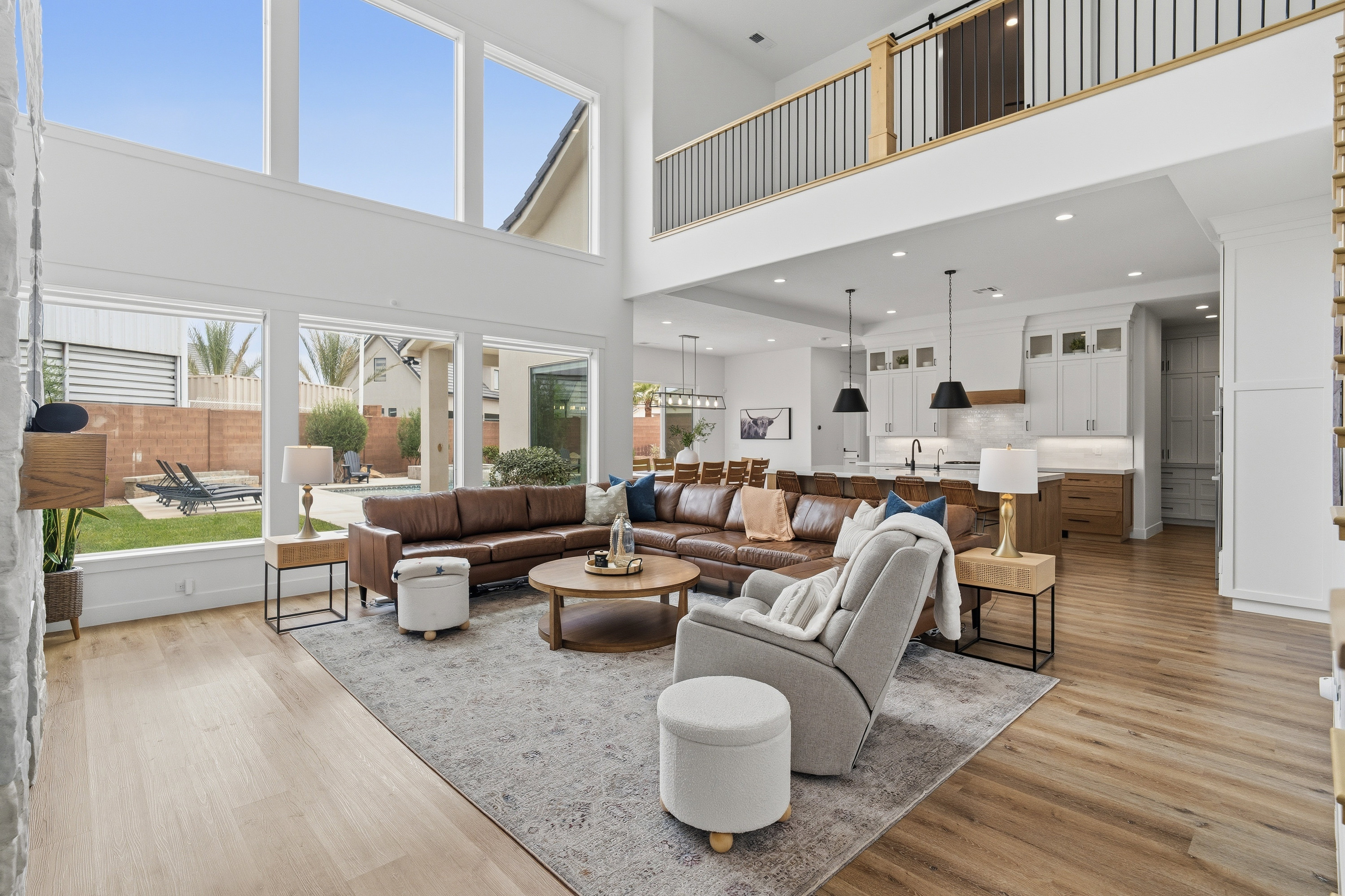 Double-height living space featuring expansive windows, wood-finish flooring, and a modern kitchen with pendant lighting and built-in cabinetry.