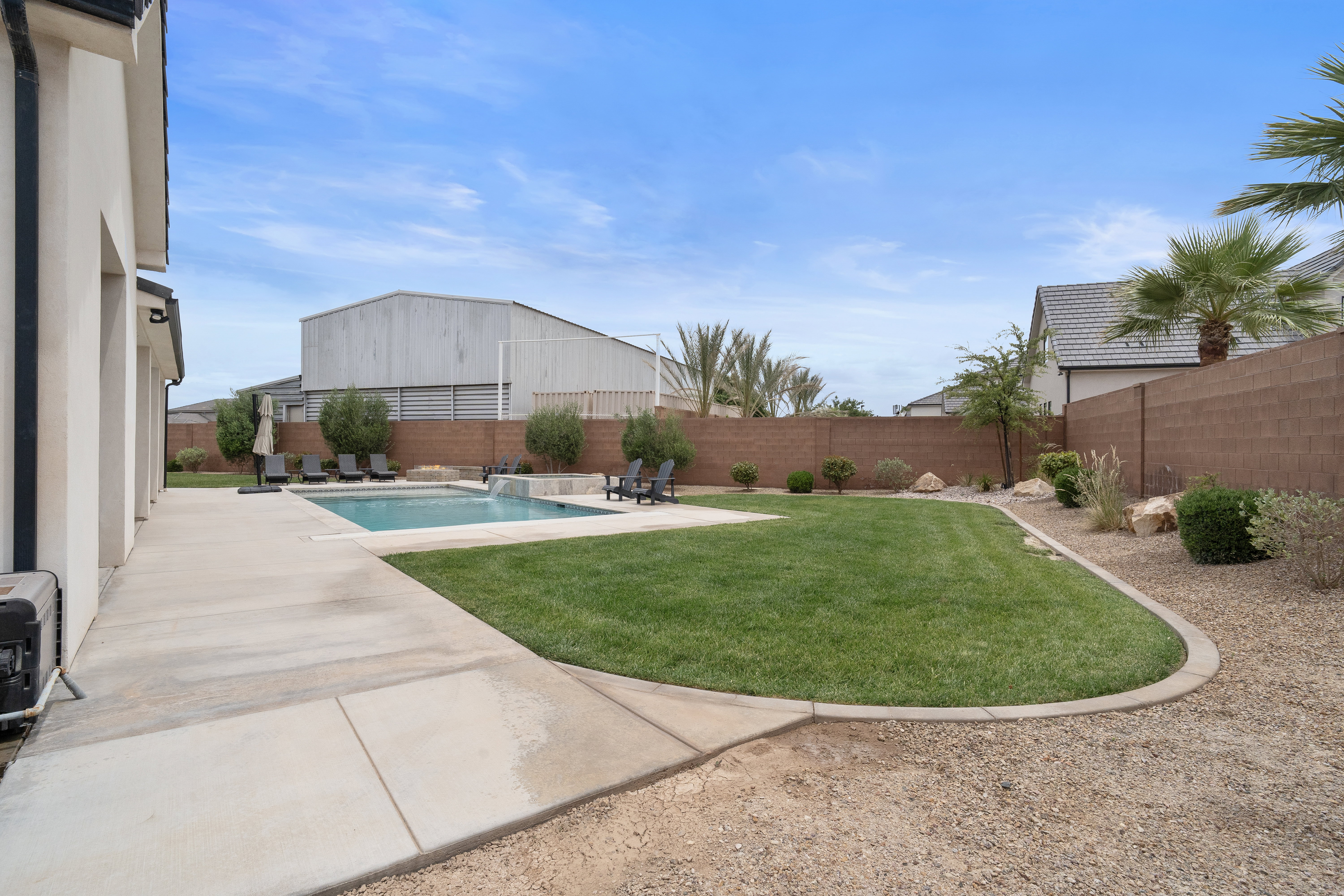 Expansive backyard featuring a rectangular swimming pool with integrated spa, a concrete patio surround, a manicured lawn area, and decorative gravel landscaping.