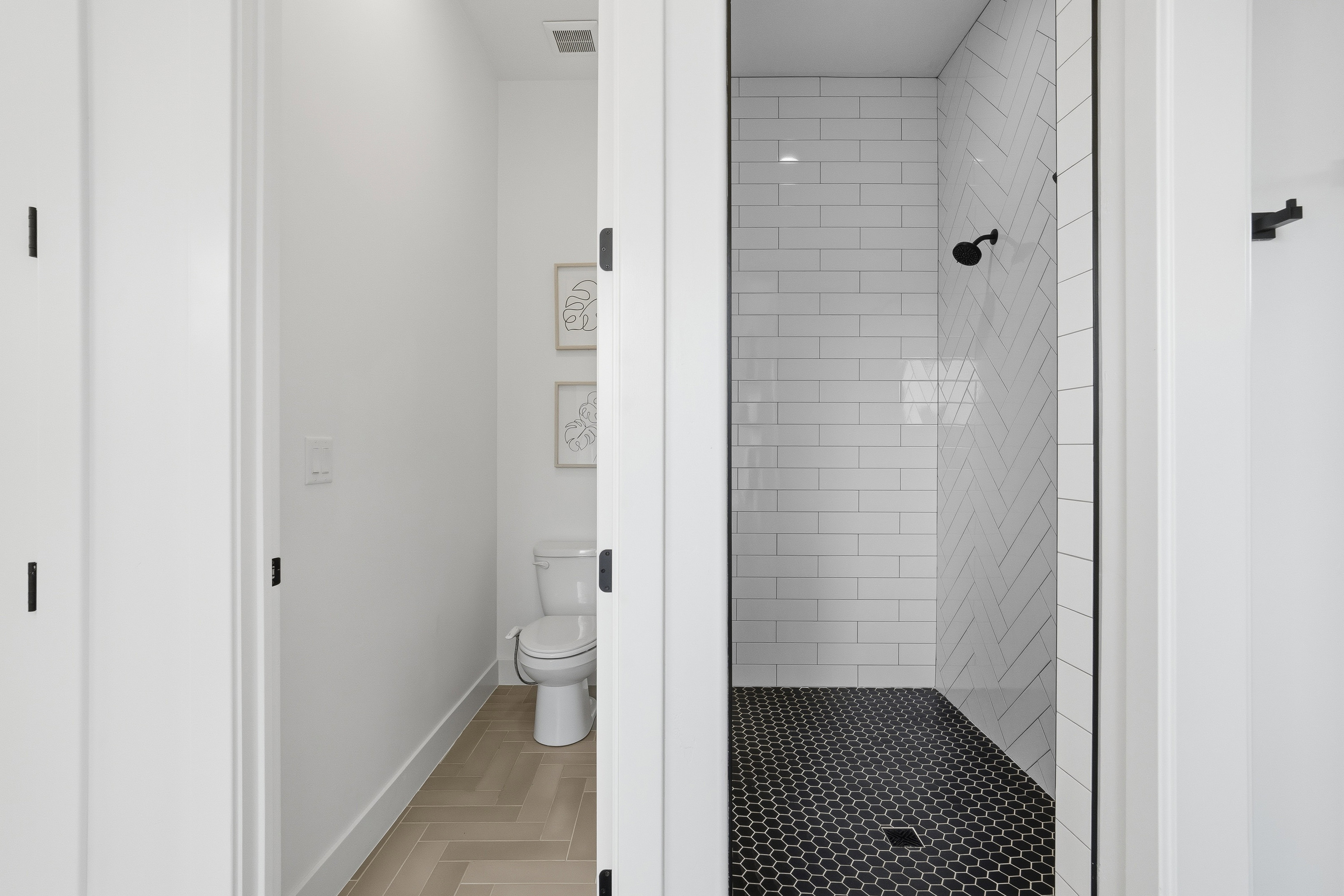 Contemporary shower stall featuring white subway tile in a herringbone pattern, a black hexagonal tile floor, and a matte black shower head.