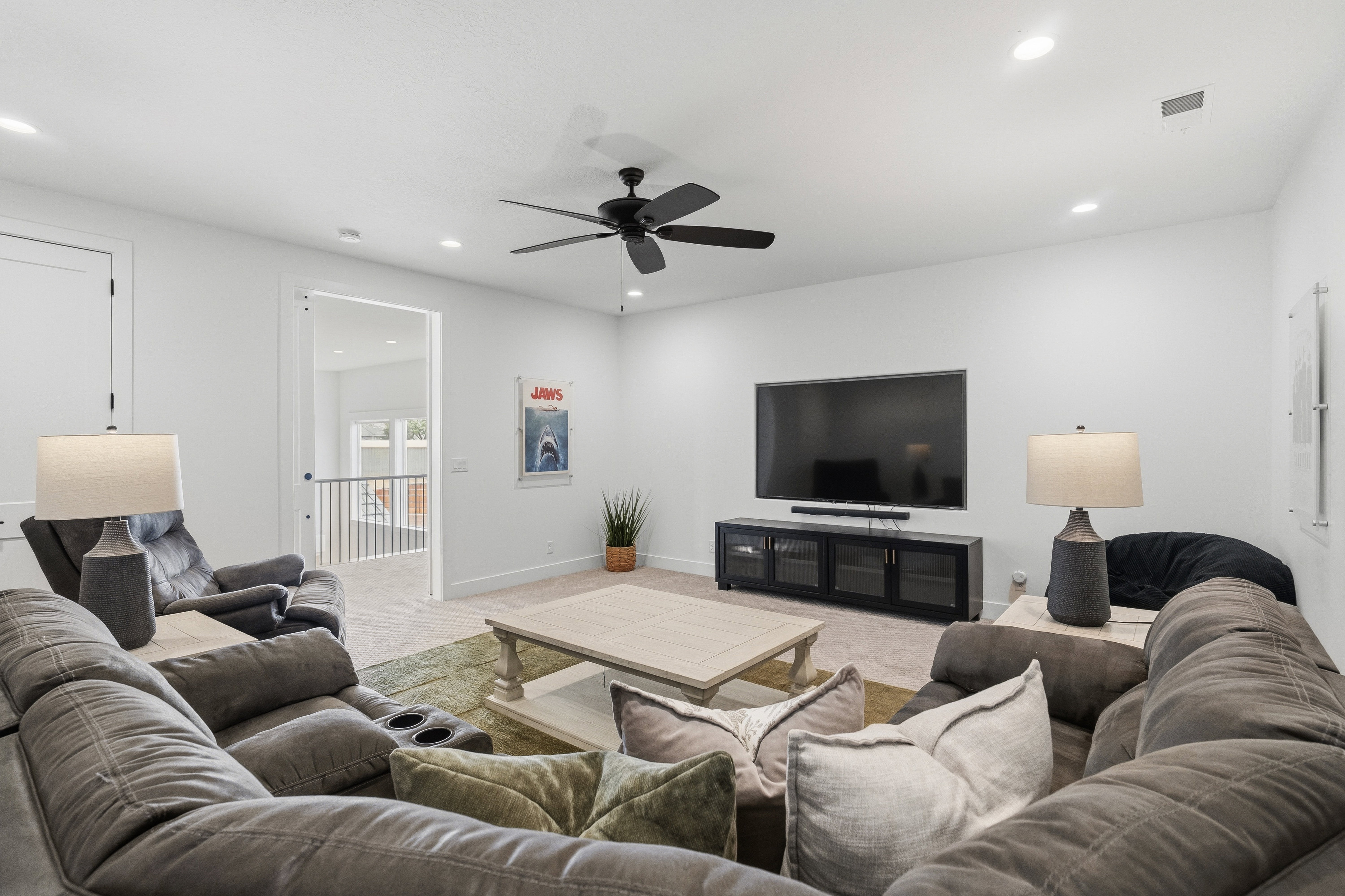 Spacious media room featuring recessed lighting, a ceiling fan, light-colored carpeting, a wall-mounted television, and a media console with glass-front cabinets.