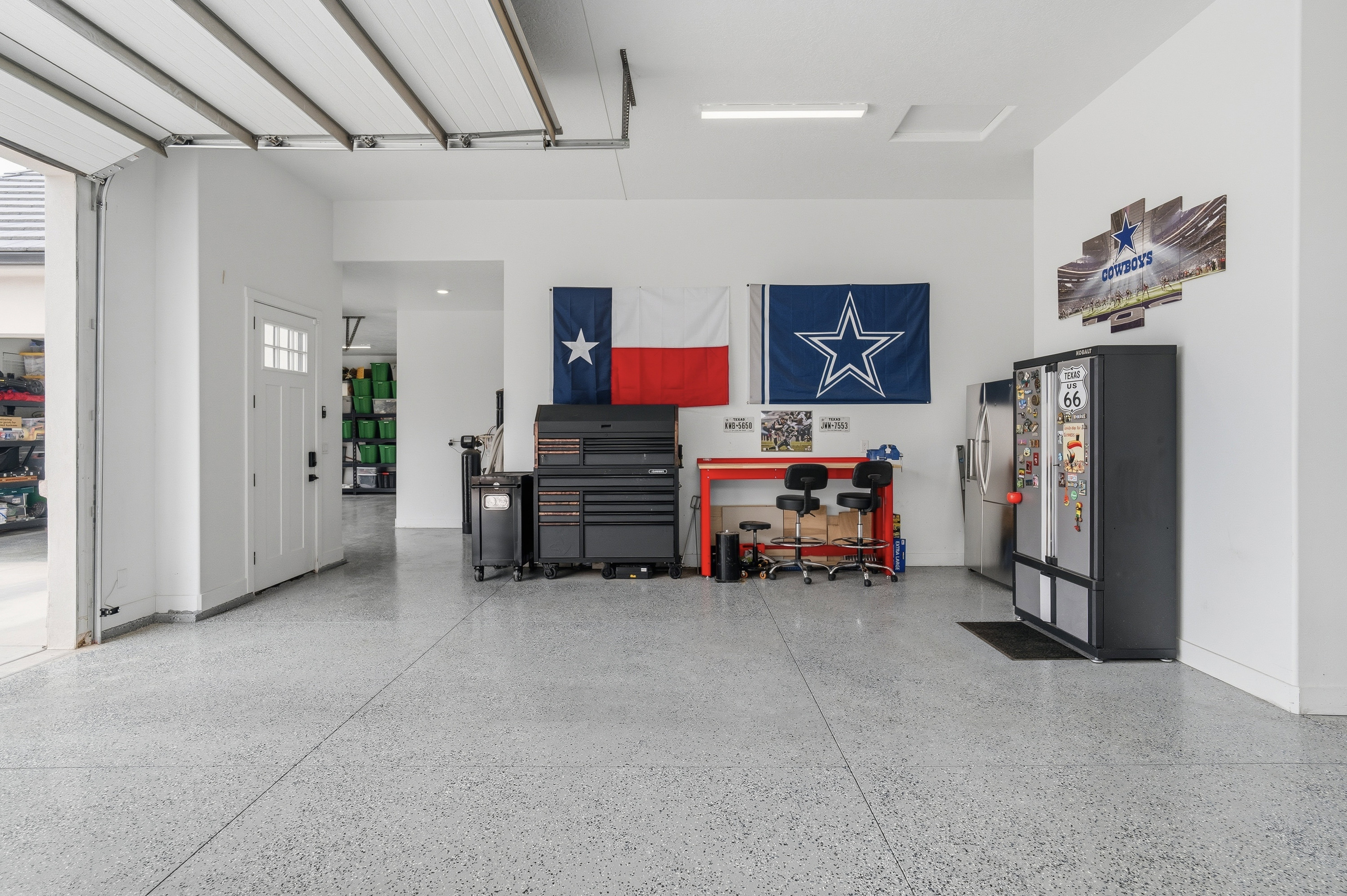 Spacious garage featuring a durable epoxy floor, white walls, overhead garage door, and a white interior door with windows.