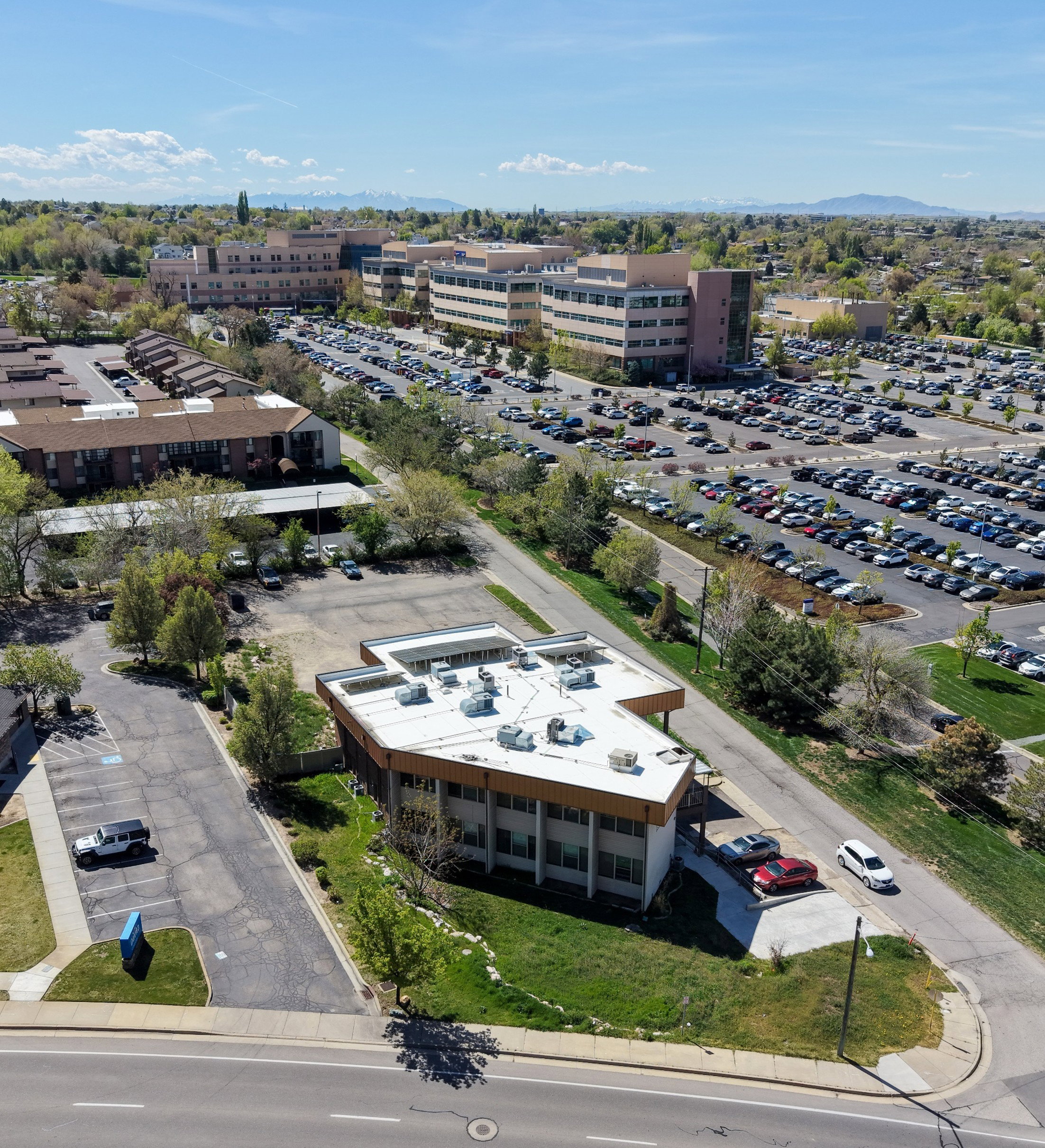Modern commercial building featuring a distinctive architectural design, ample on-site parking, a flat roof, and a surrounding green space with mature trees