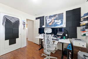 Room featuring wood-finish flooring, white walls, and a built-in wall installation of sound-absorbing panels
