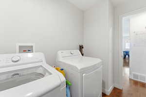 Dedicated laundry area featuring white walls and wood-finish flooring