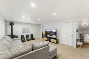 Carpeted living area featuring a black wood stove with pipe, recessed lighting, and a window with plantation shutters