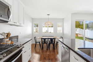 Kitchen featuring white cabinetry, dark stone countertops, stainless steel appliances, and wood-finish flooring