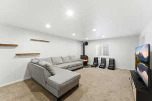 Spacious living area featuring neutral carpeting, recessed lighting, and a modern wood-burning stove with a visible flue