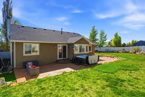 Spacious backyard featuring a large green lawn, a paver patio, and an integrated hot tub