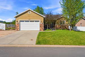 Single-story residence featuring a two-car garage with a white sectional door, a stucco and stone veneer exterior, a concrete driveway, and a front lawn with mature trees