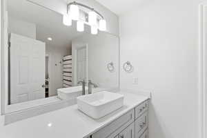 Modern vanity featuring a vessel sink, a light-toned countertop, and light gray cabinetry with brushed nickel hardware