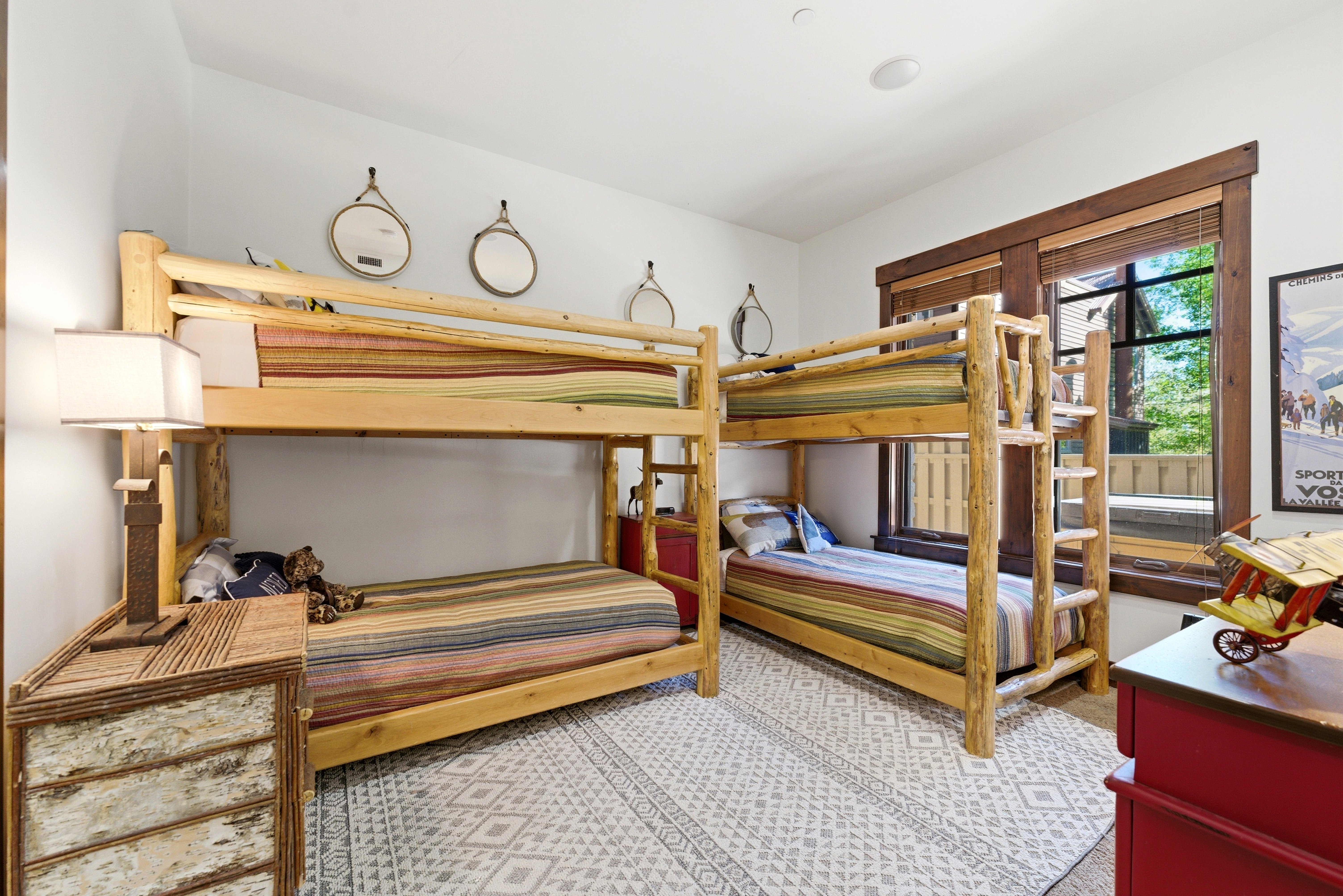 Bedroom featuring two bunk beds with natural wood frames, a large window with wood trim, and a patterned area rug