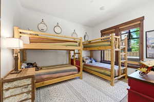 Bedroom featuring two bunk beds with natural wood frames, a large window with wood trim, and a patterned area rug