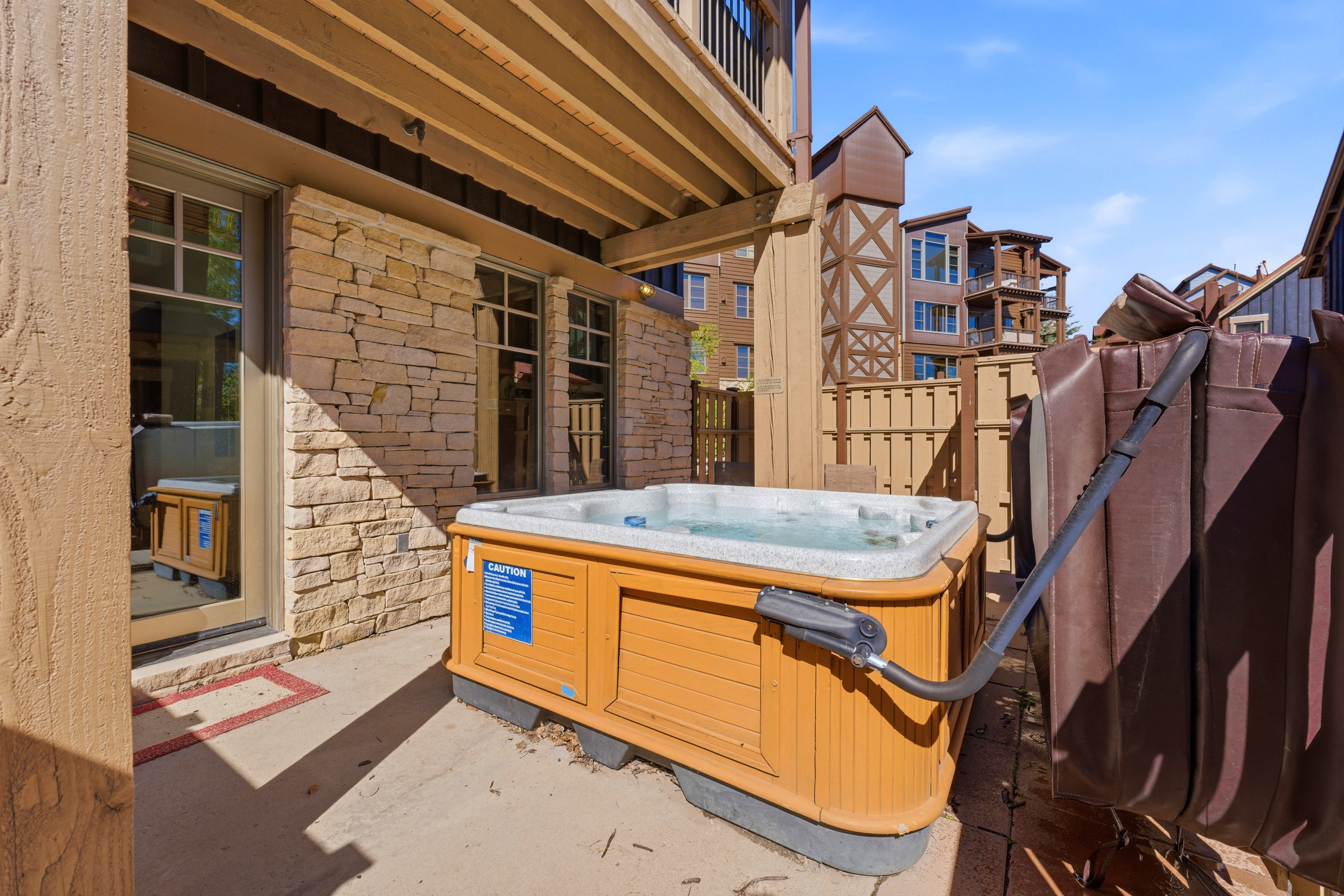 Patio with a built-in hot tub, stone exterior wall, and multiple windows