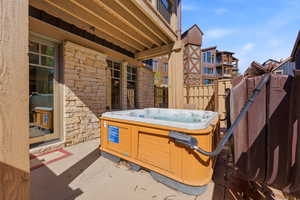 Patio with a built-in hot tub, stone exterior wall, and multiple windows