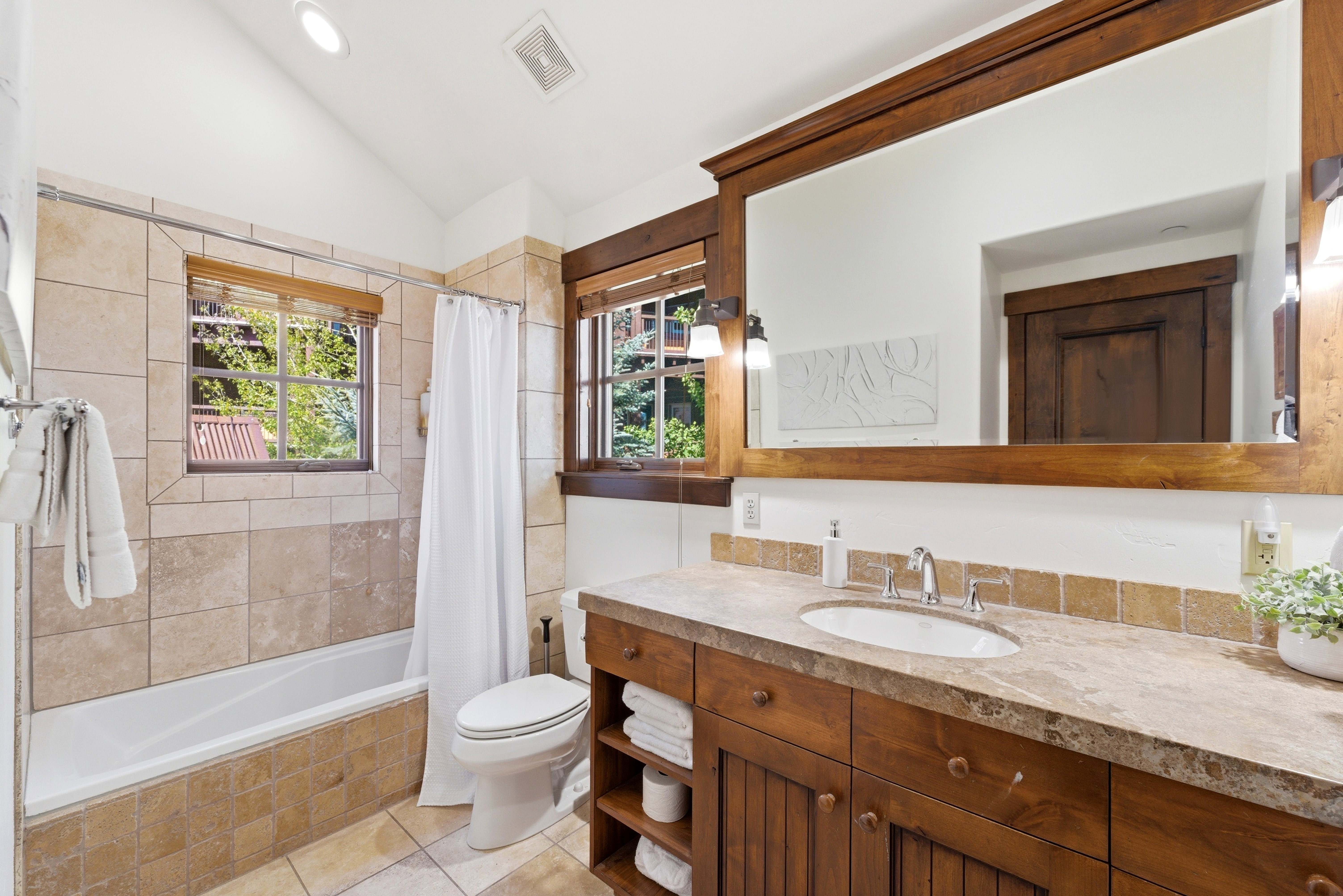 Bathroom featuring a full vanity with wood-finish cabinetry, an oval undermount sink, and a stone countertop