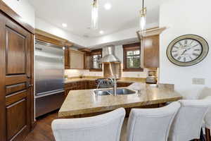 Gourmet kitchen featuring a stainless steel Viking refrigerator, granite countertops, wood-finish cabinetry, and a built-in stainless steel range hood
