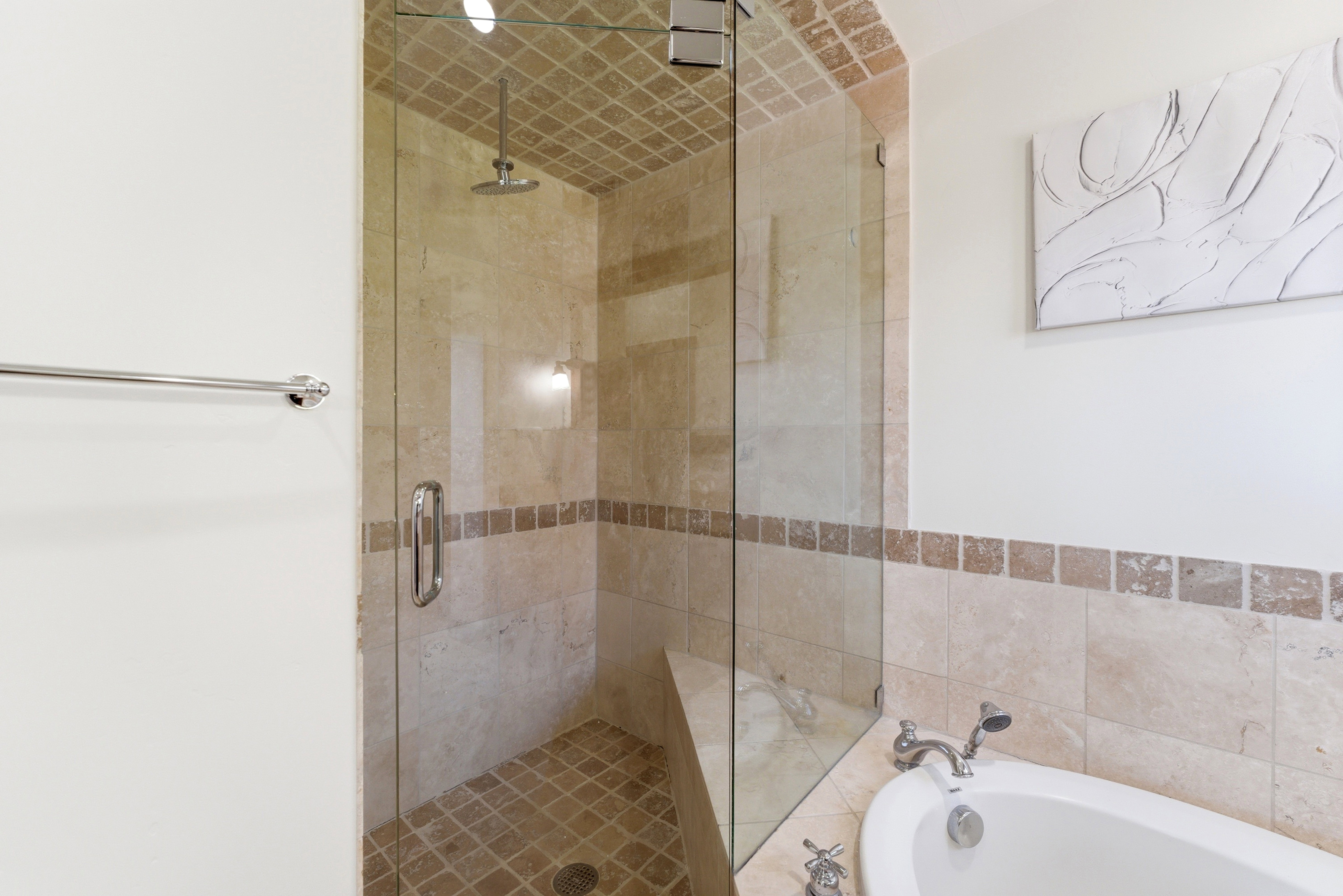 Glass-enclosed shower featuring a rainfall showerhead, built-in bench, and floor-to-ceiling tile work, complemented by a soaking tub with polished chrome fixtures and a natural stone tile surround