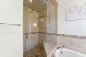 Glass-enclosed shower featuring a rainfall showerhead, built-in bench, and floor-to-ceiling tile work, complemented by a soaking tub with polished chrome fixtures and a natural stone tile surround
