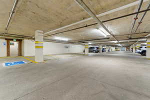 Spacious underground parking area featuring concrete flooring, exposed pipework, and fluorescent lighting