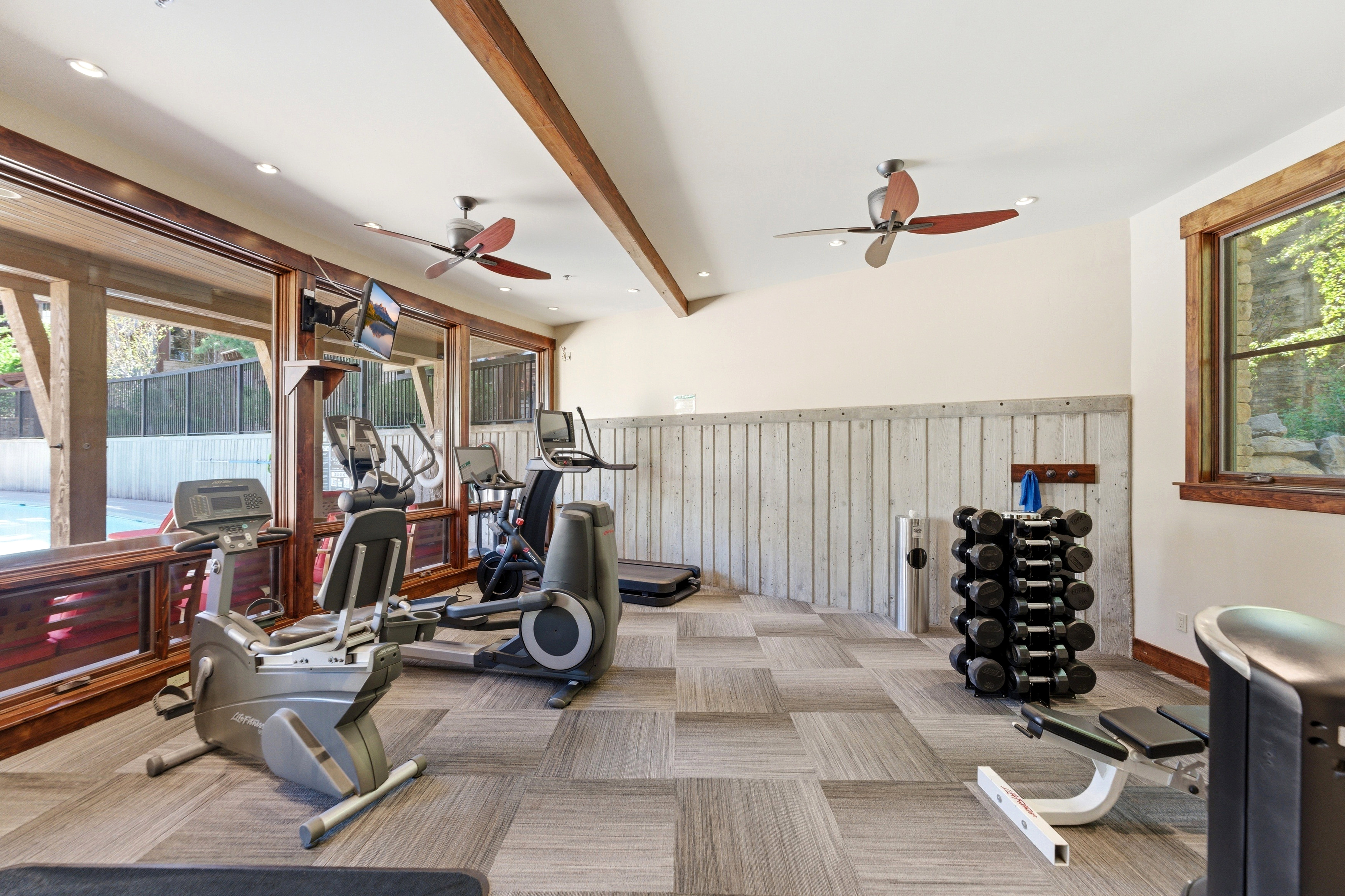 Dedicated fitness area featuring extensive natural light from large windows, exposed wood beams, and patterned carpet tile flooring