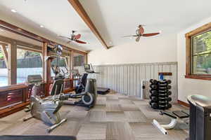 Dedicated fitness area featuring extensive natural light from large windows, exposed wood beams, and patterned carpet tile flooring