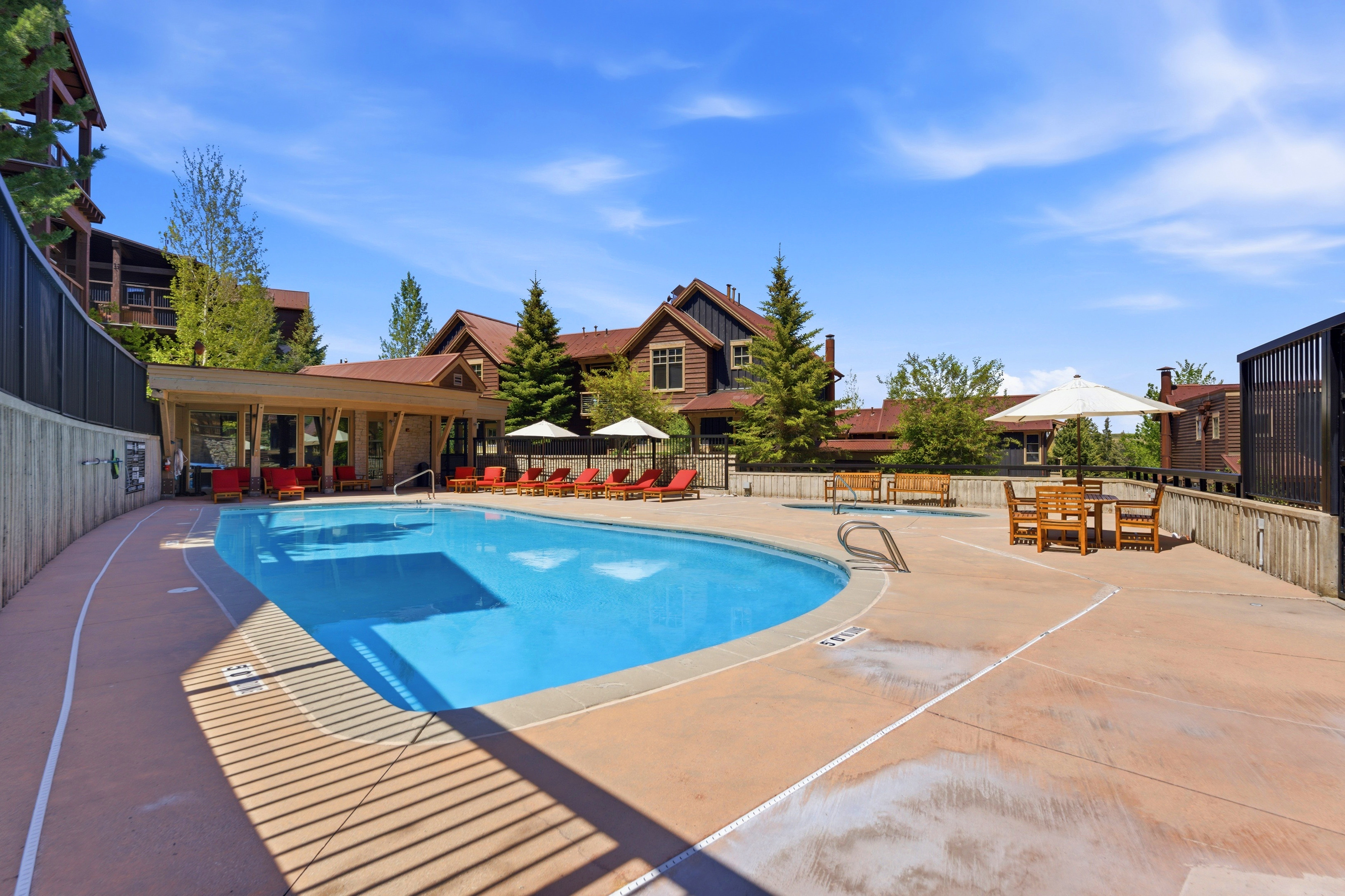 Resort-style outdoor swimming pool with integrated spa, expansive concrete decking, and a covered lounge area