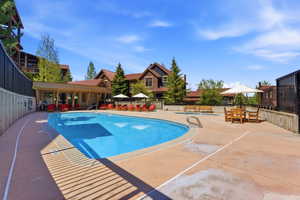 Resort-style outdoor swimming pool with integrated spa, expansive concrete decking, and a covered lounge area