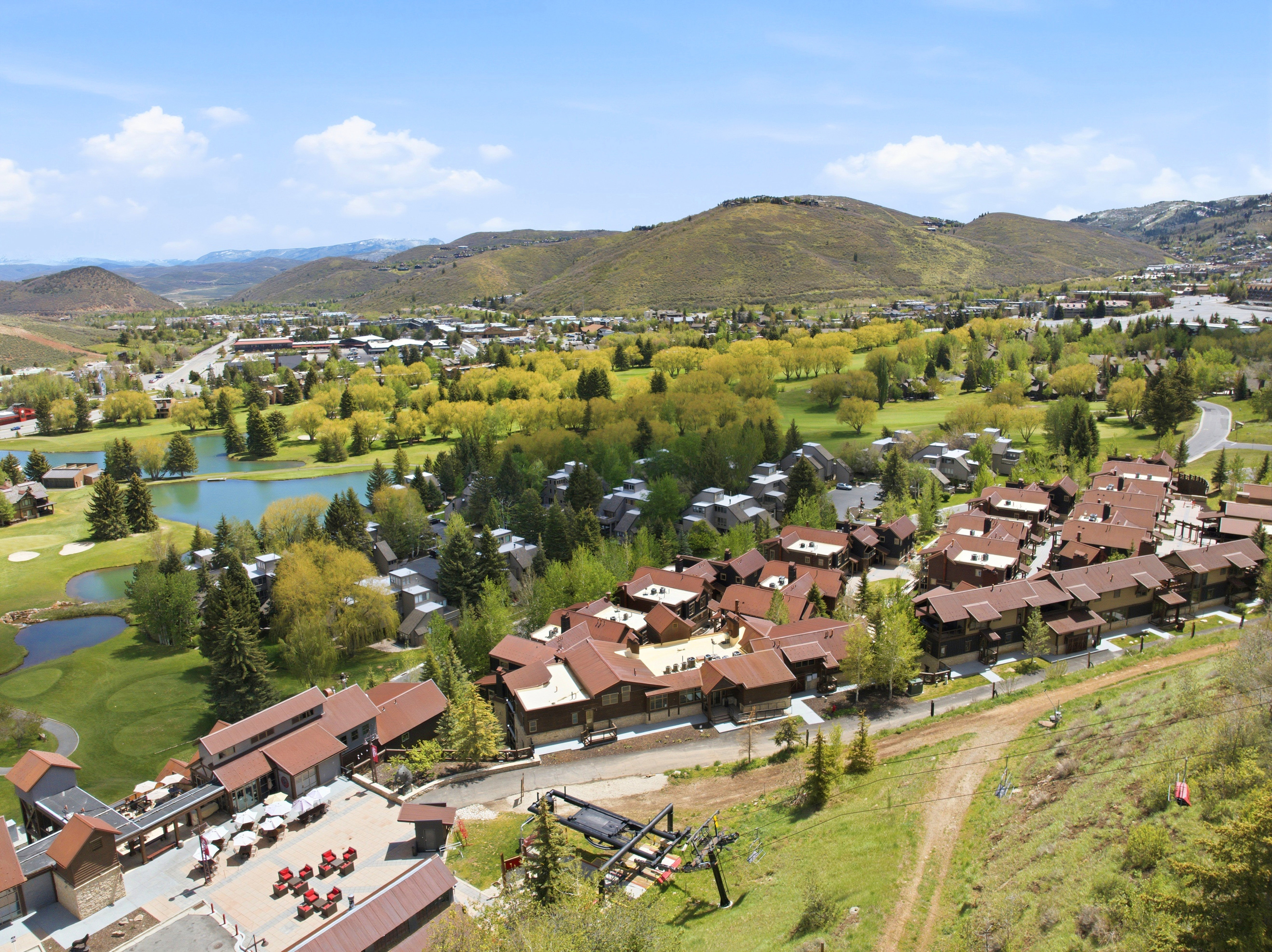 Expansive aerial panorama showcasing a multi-building complex with brown roofs and natural wood siding, surrounded by mature trees