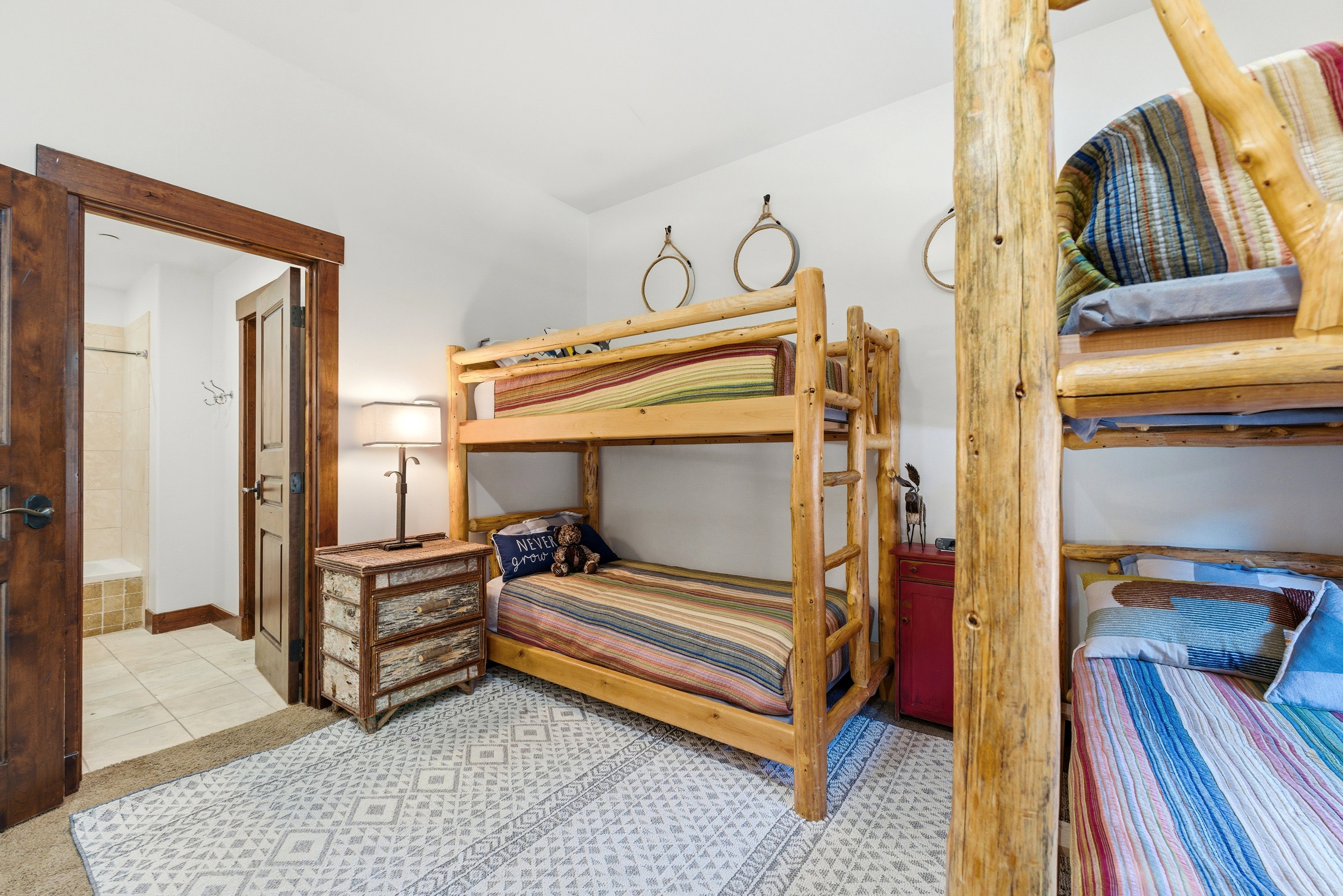 Bedroom featuring two wood-frame bunk beds, a patterned area rug, and a wood-paneled door opening to a bathroom with tiled flooring and a shower