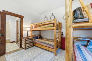 Bedroom featuring two wood-frame bunk beds, a patterned area rug, and a wood-paneled door opening to a bathroom with tiled flooring and a shower