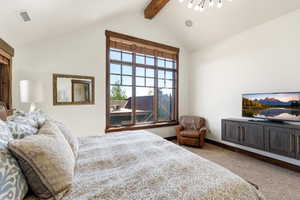 Vaulted ceiling with exposed wood beam, large multi-pane window with wood trim, wall-mounted media console, and recessed lighting fixtures
