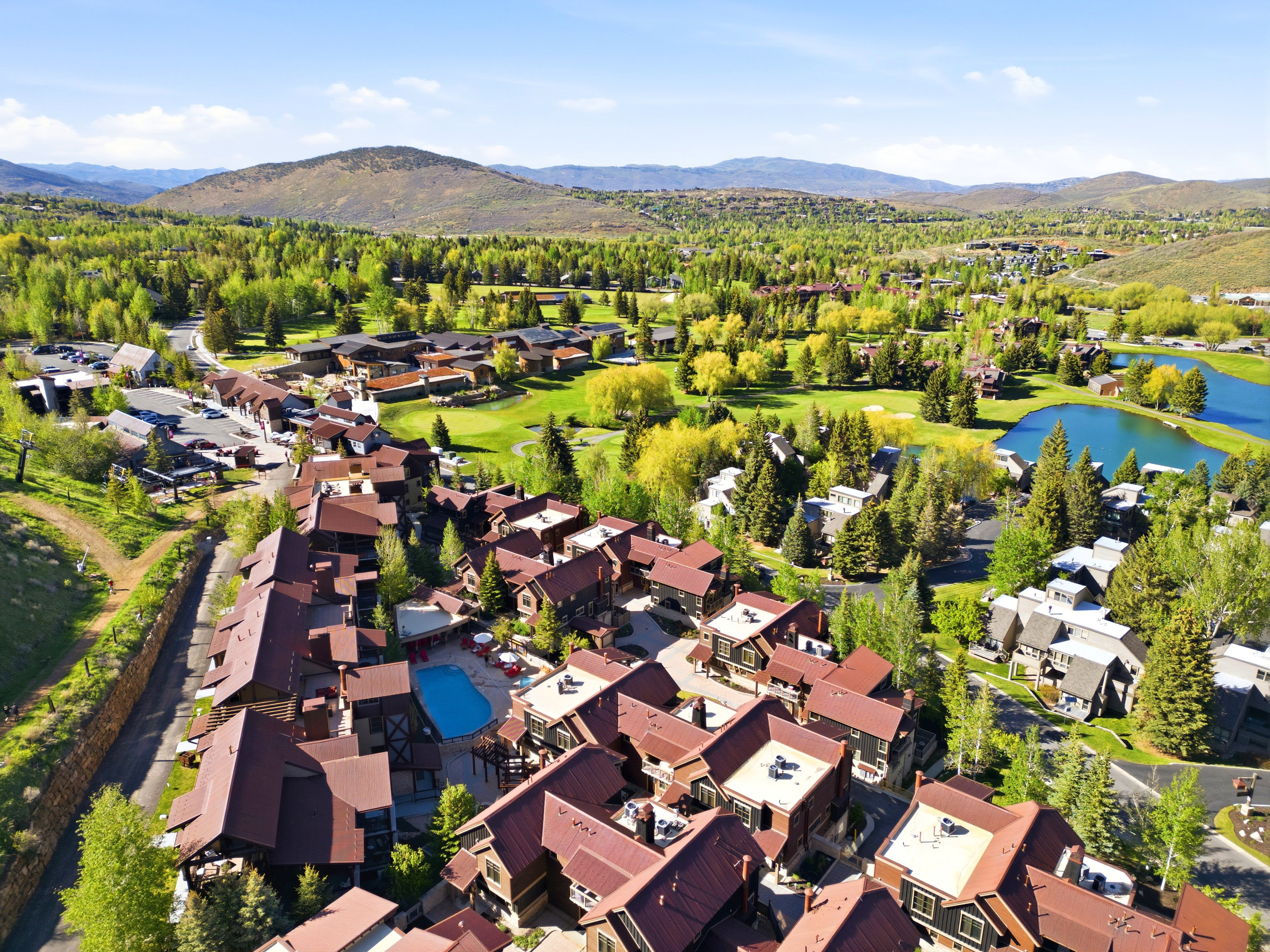 Expansive aerial capturing a community with various architectural styles, including multi-story residences with red-hued roofs and brown siding