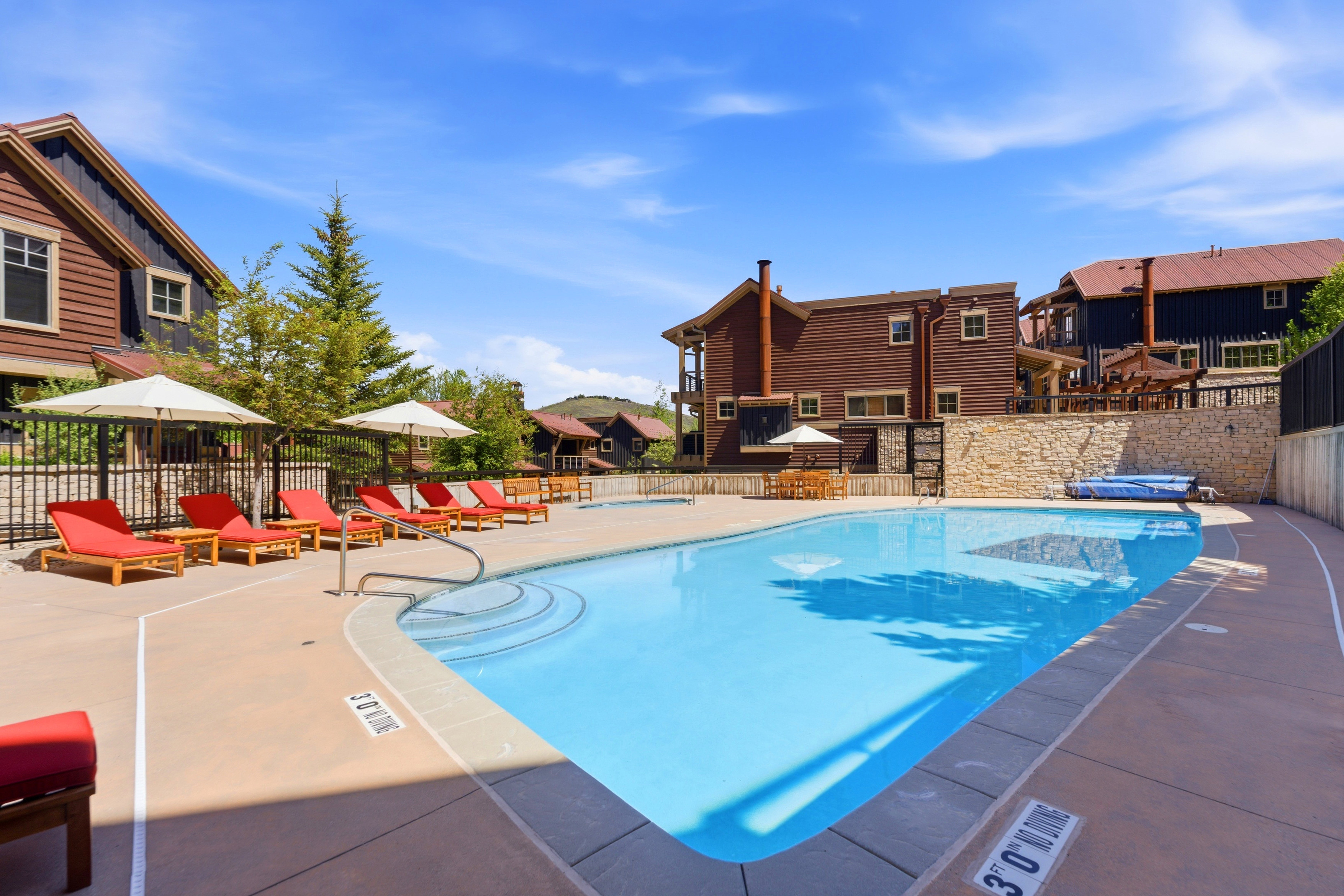 Community swimming pool featuring concrete decking, perimeter fencing, and mature landscaping