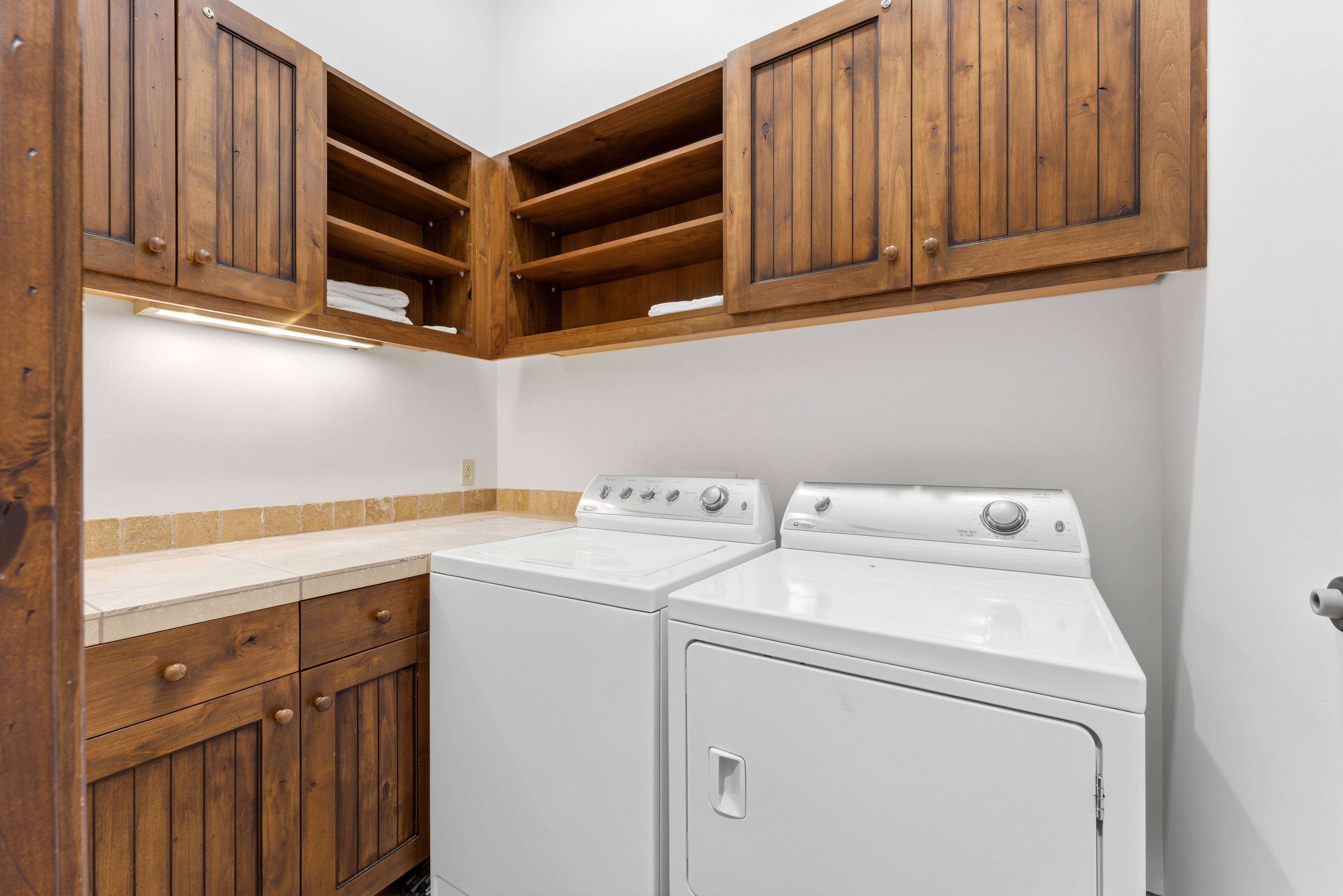 Laundry room featuring wood cabinetry, open shelving, stone countertop, and under-cabinet lighting