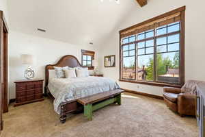 Bedroom featuring a vaulted ceiling with exposed wood beams, a large picture window with wood trim, and textured carpeting
