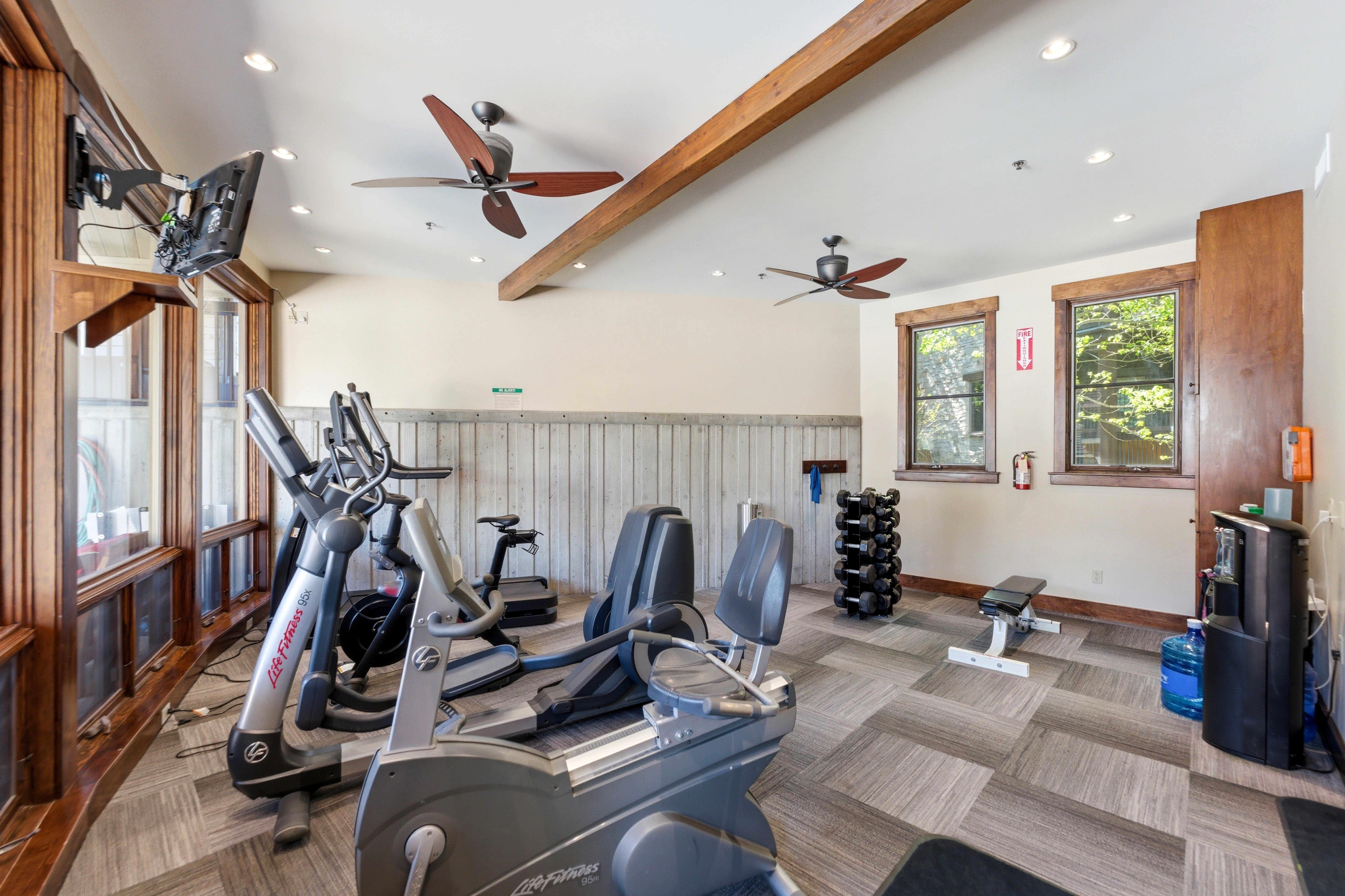 Fitness area featuring geometric patterned carpet, exposed wooden ceiling beams, recessed lighting, and dual ceiling fans