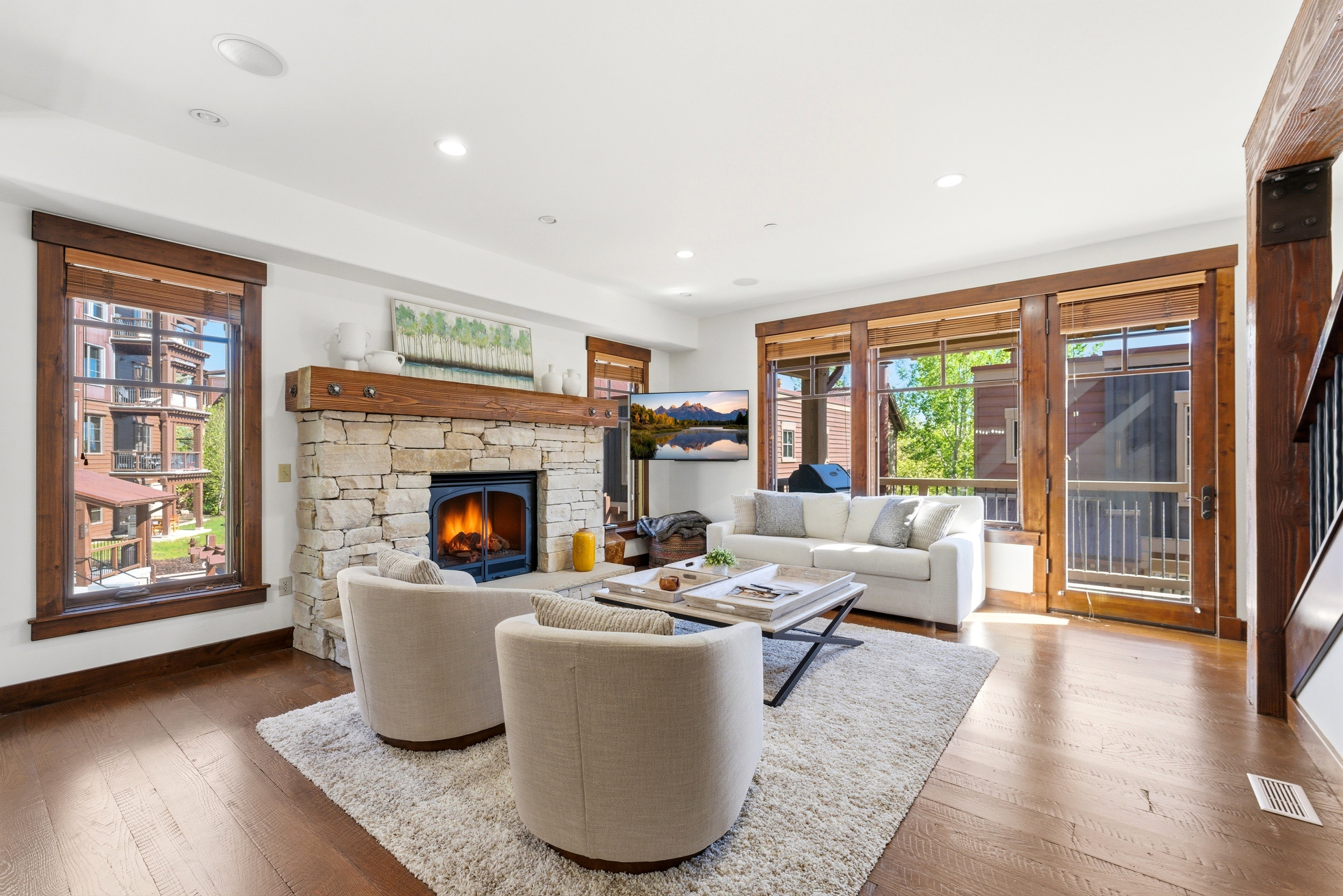 Living area featuring a stone fireplace with a wood mantle, wood-finish flooring, recessed lighting, and multiple windows with wood trim